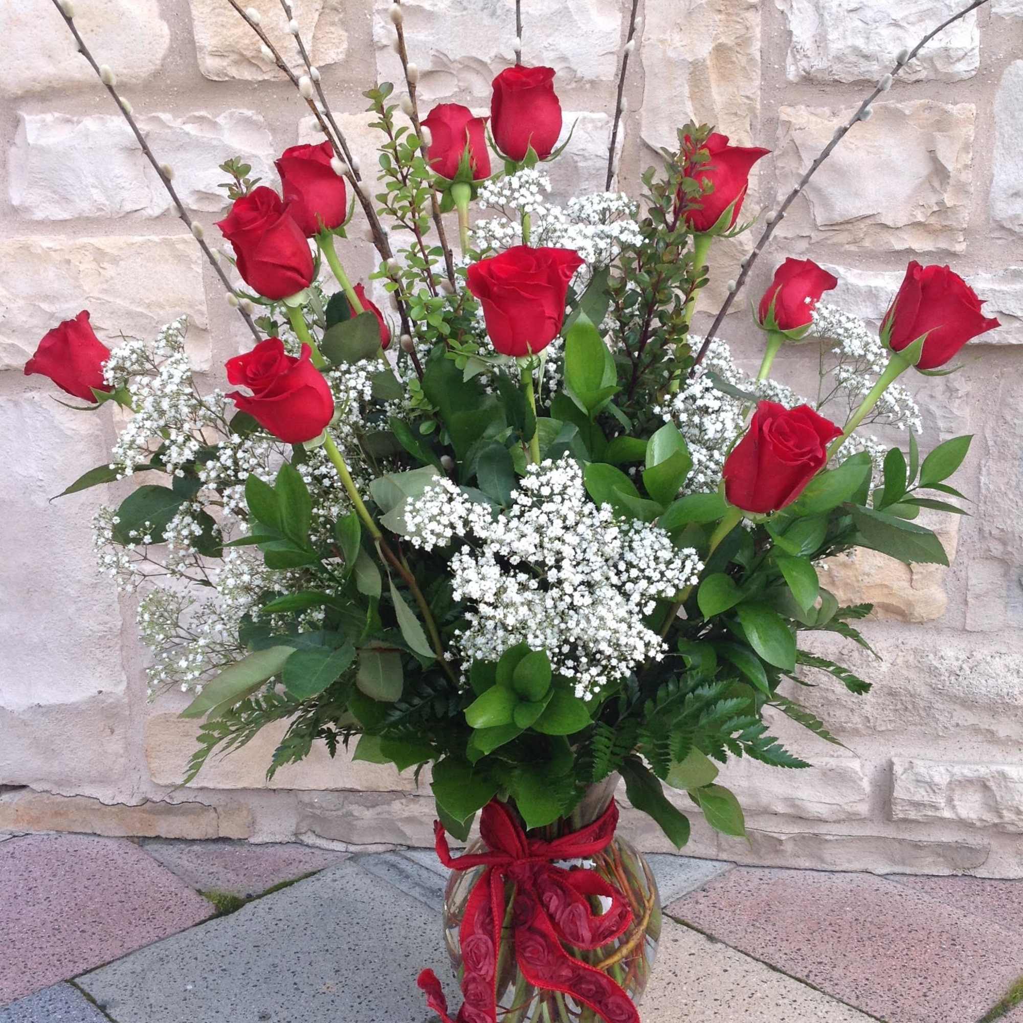 Red roses and baby's breath in a glass vase with a red ribbon