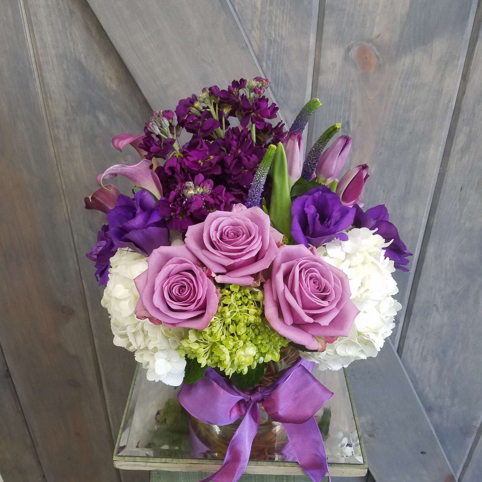Purple and white floral arrangement with roses, hydrangeas, and calla lilies in a vase