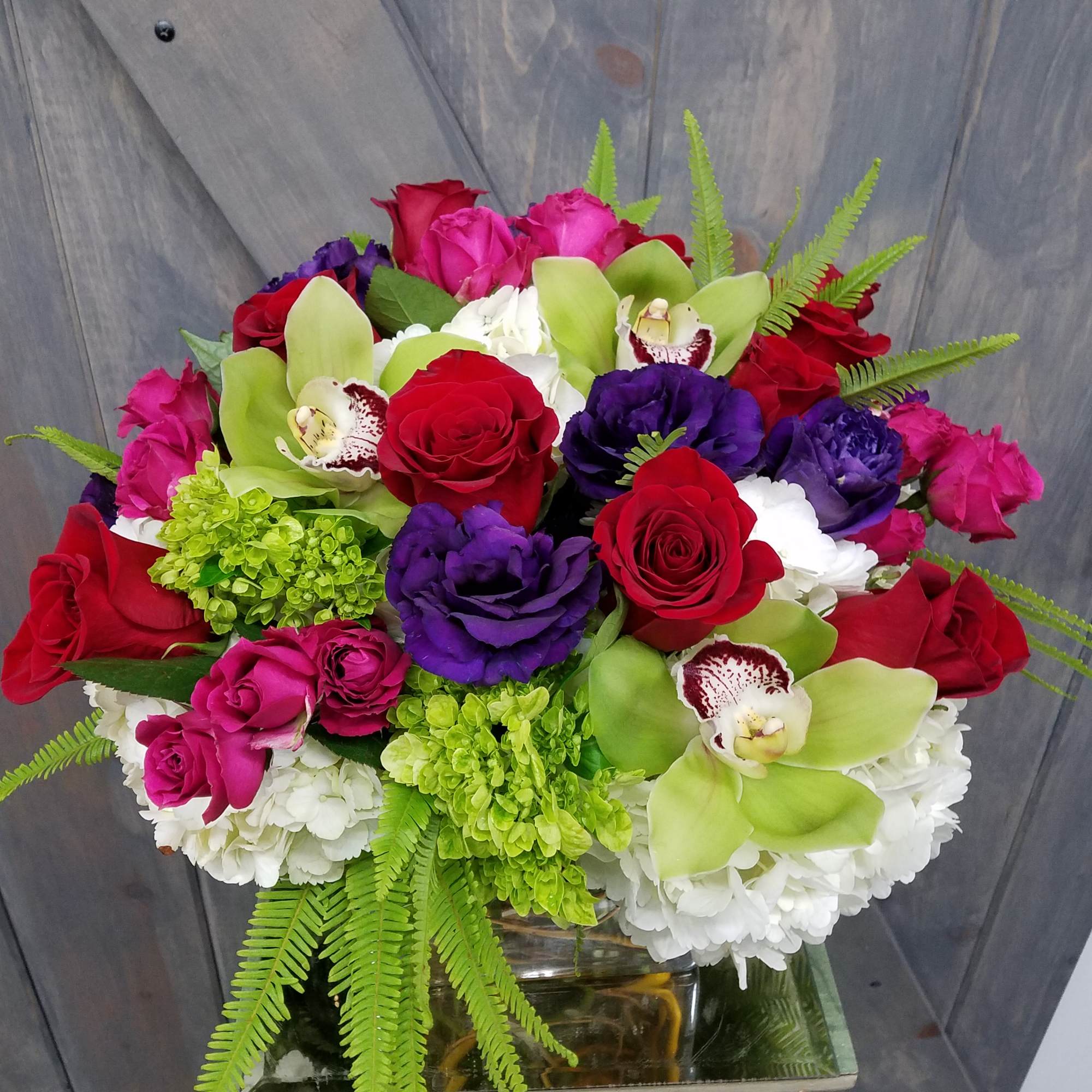 Bouquet of red and pink roses with green orchids and purple blooms in a glass vase