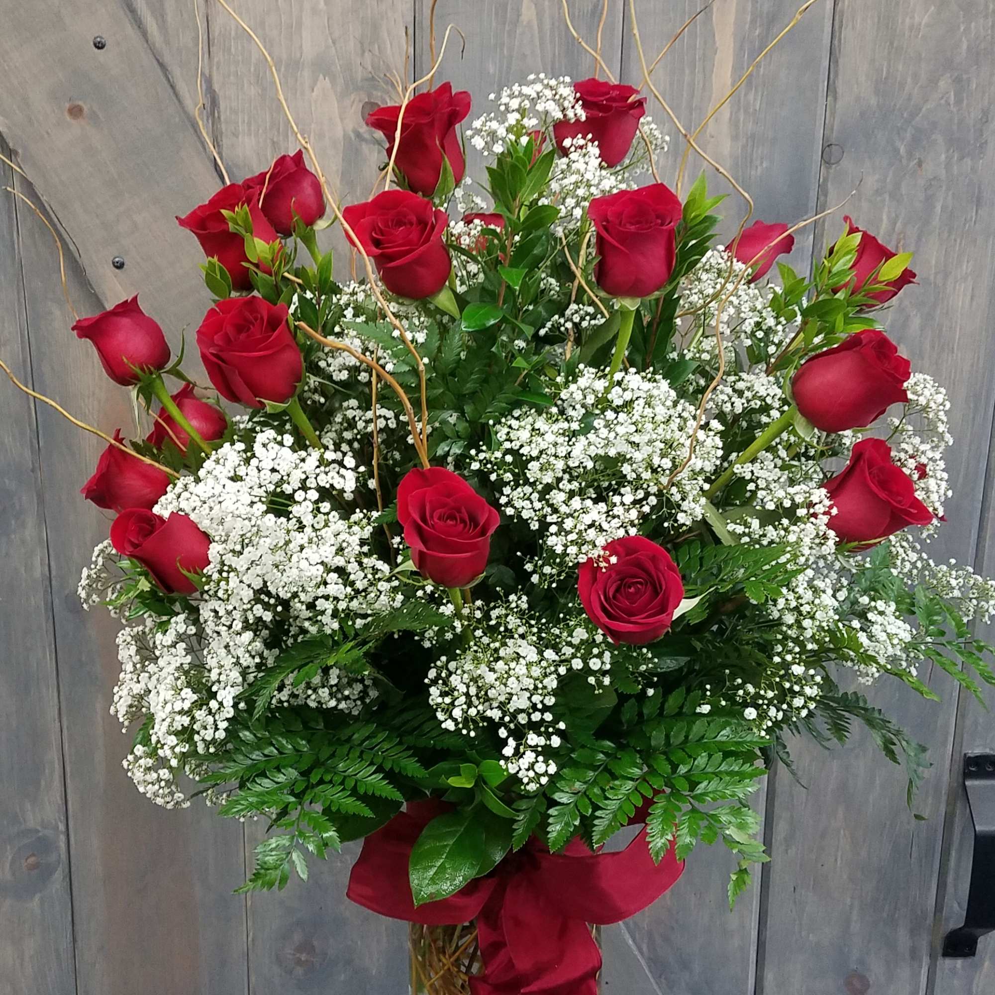 Red roses arranged in a tall vase with white baby's breath