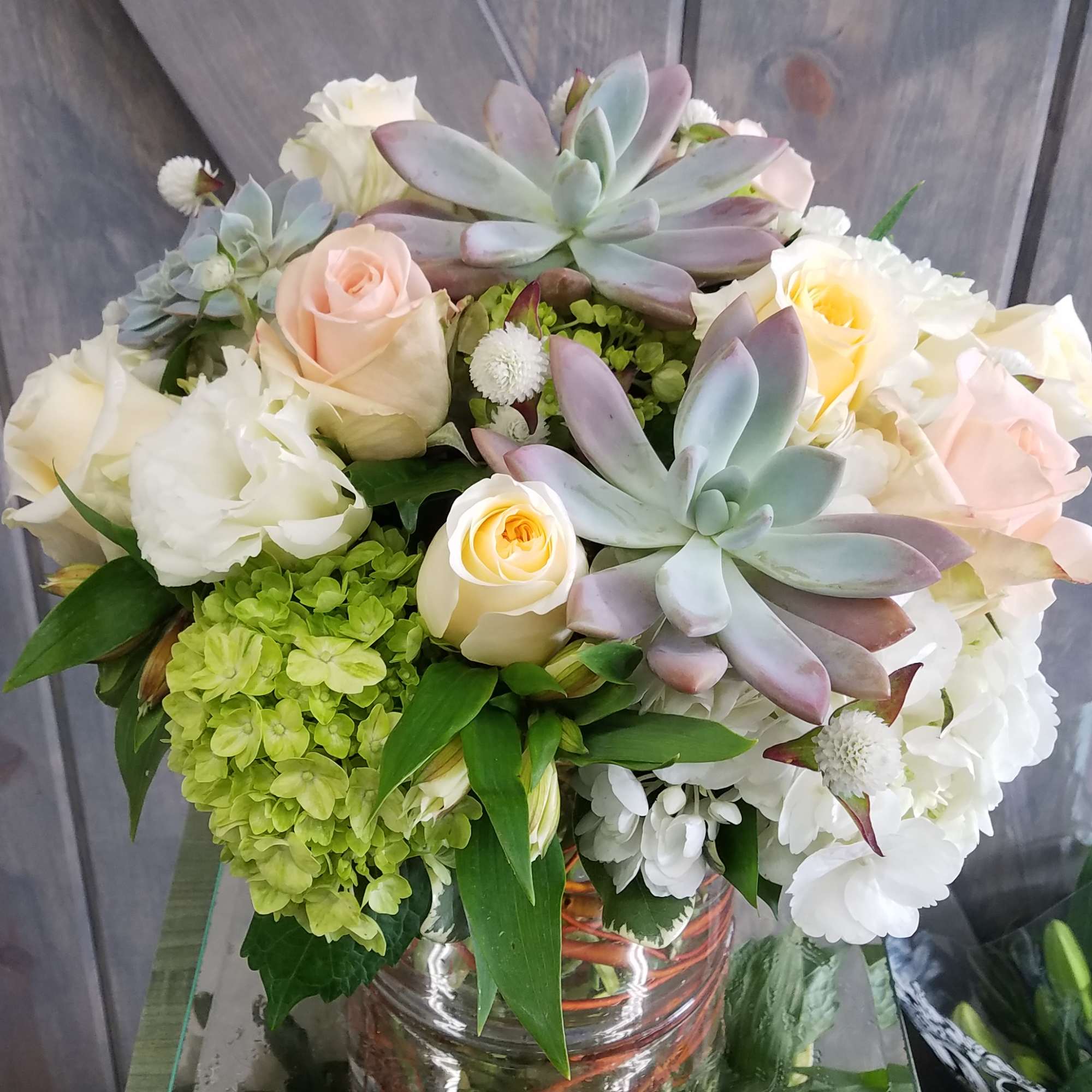 Bouquet of roses, hydrangeas, and succulents in a glass vase