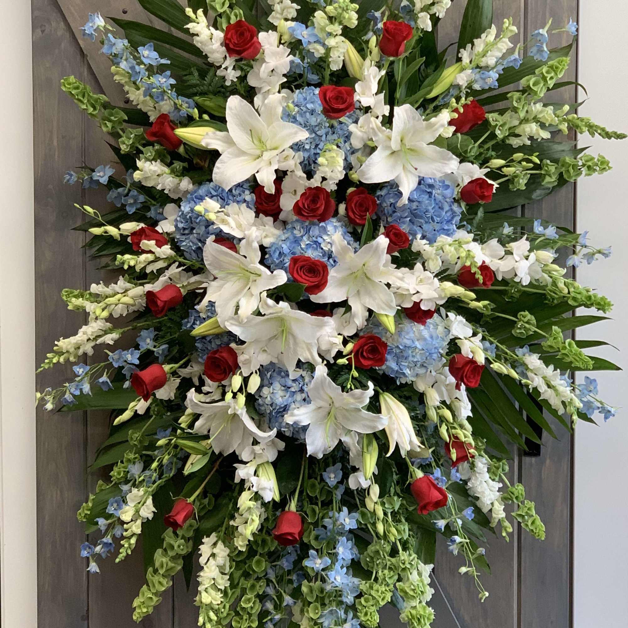 Large standing floral spray with red roses, white lilies, and blue hydrangeas