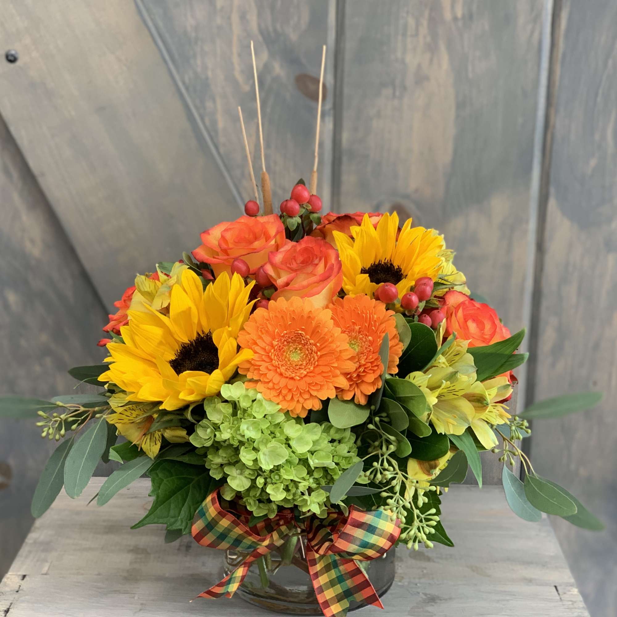 Bright mixed bouquet with sunflowers, orange roses, and gerbera daisies in a glass vase