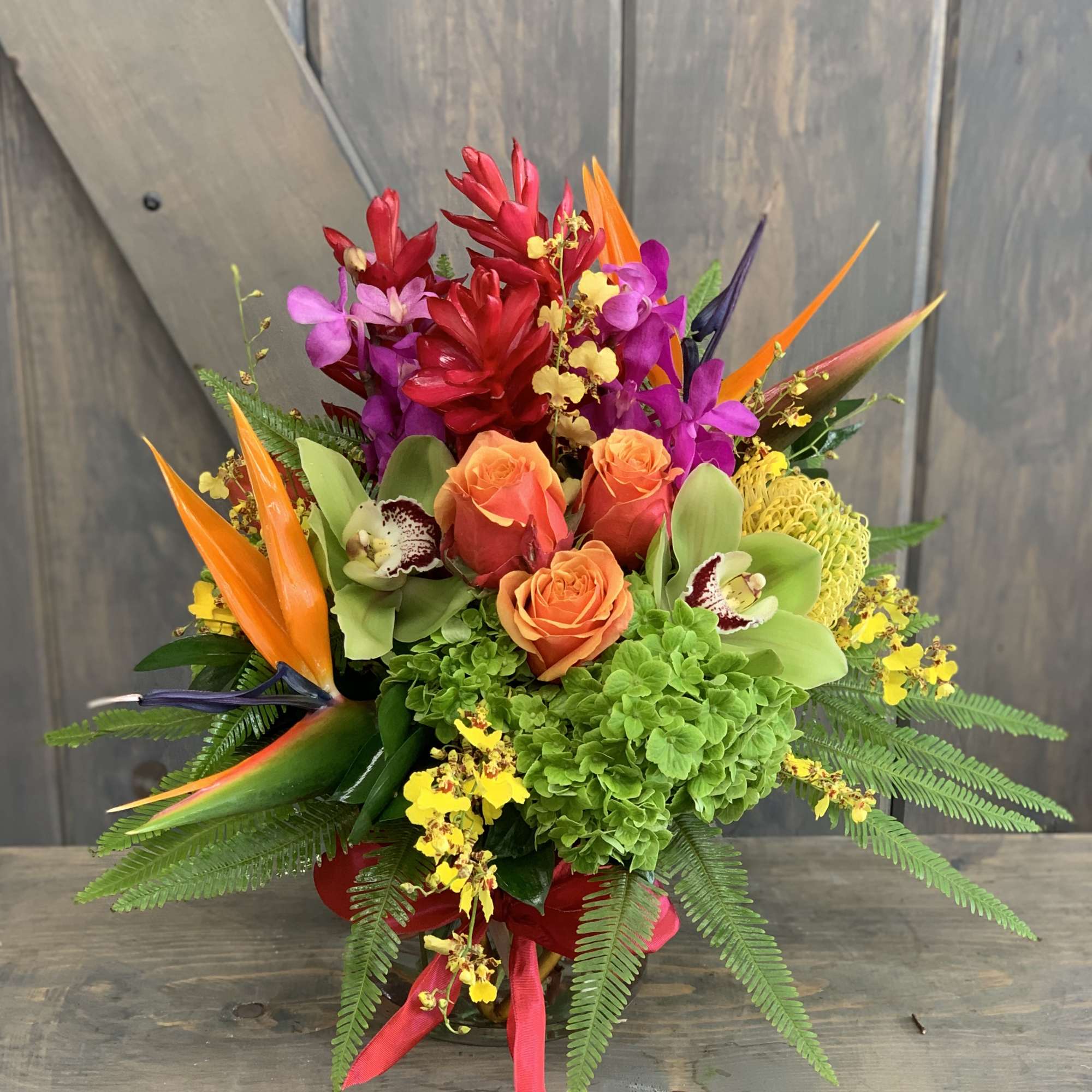 Tropical bouquet with orange roses, orchids, and bird-of-paradise in a vase