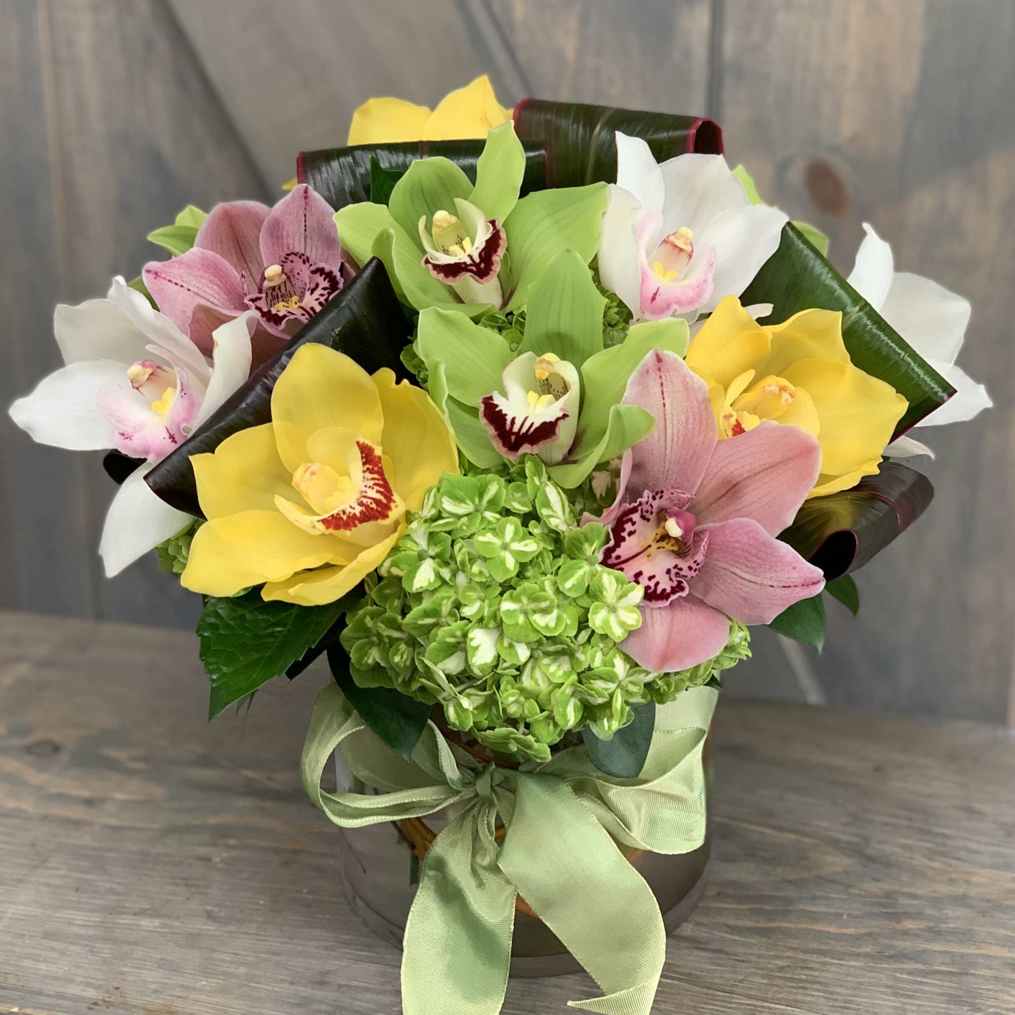 Bouquet of yellow, pink, white, and green orchids in a vase with a ribbon