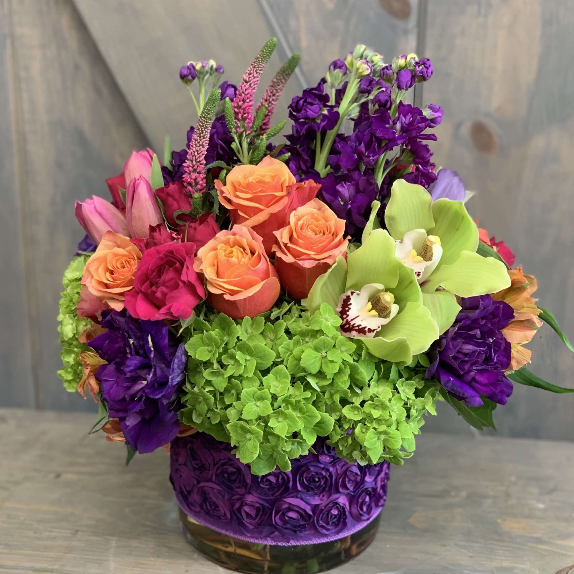 Colorful bouquet with roses, orchids, and hydrangeas in a purple vase