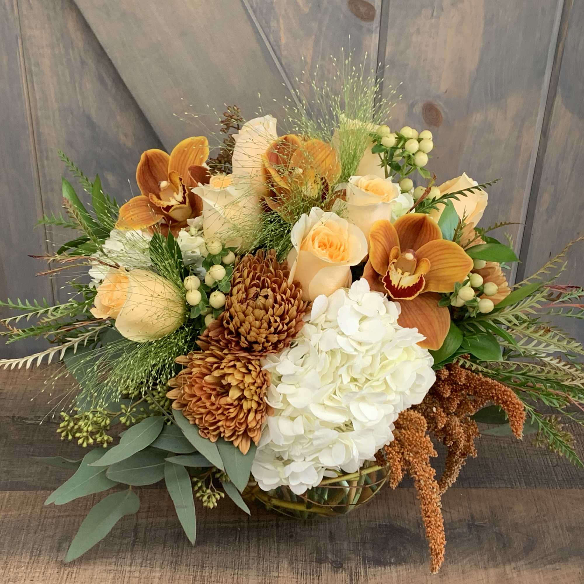 Orange and cream floral arrangement with roses, orchids, and hydrangea in a low basket