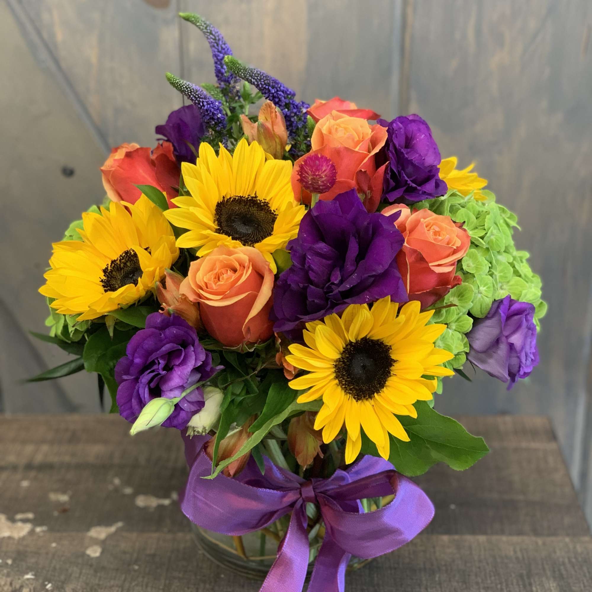 Colorful bouquet with sunflowers, roses, and purple blooms in a glass vase