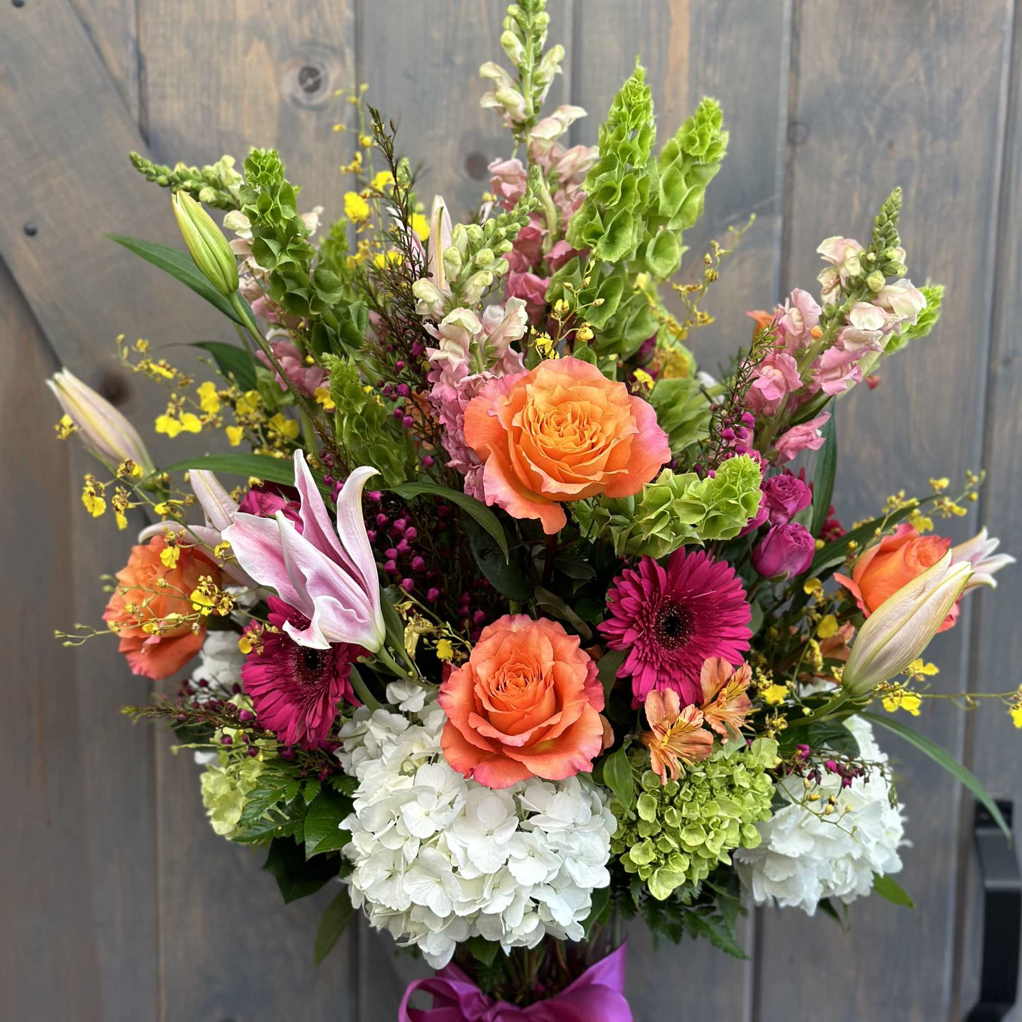 Mixed bouquet with orange roses, pink lilies, and white hydrangeas in a glass vase