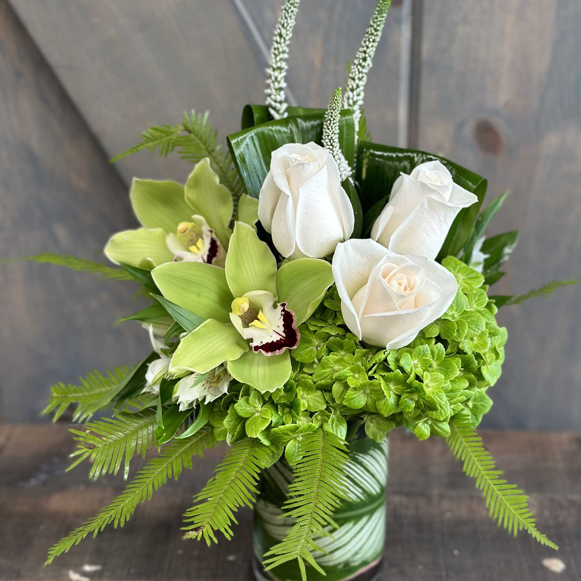 White roses and green orchids arranged in a glass vase