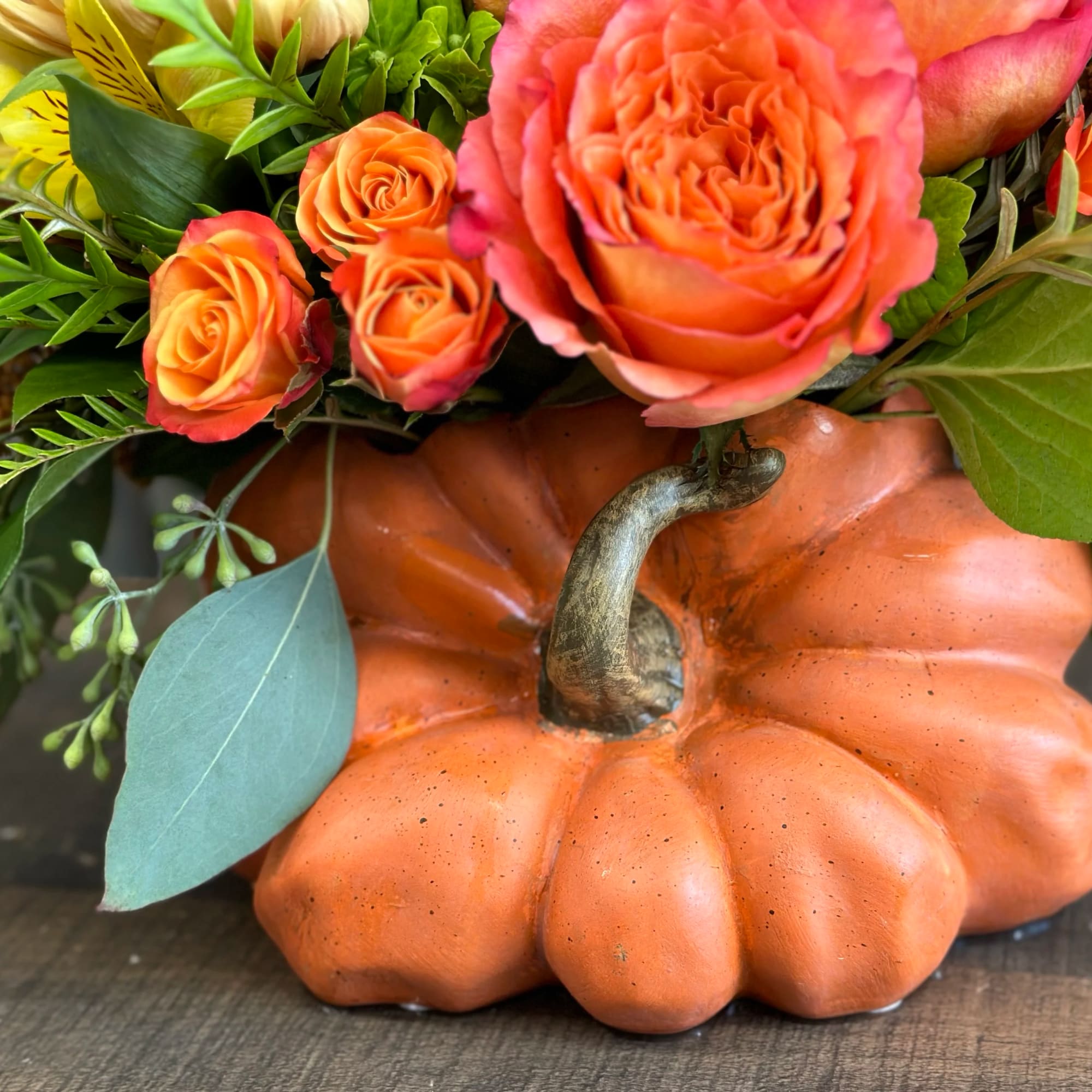 Orange roses arranged in a pumpkin container with mixed greenery