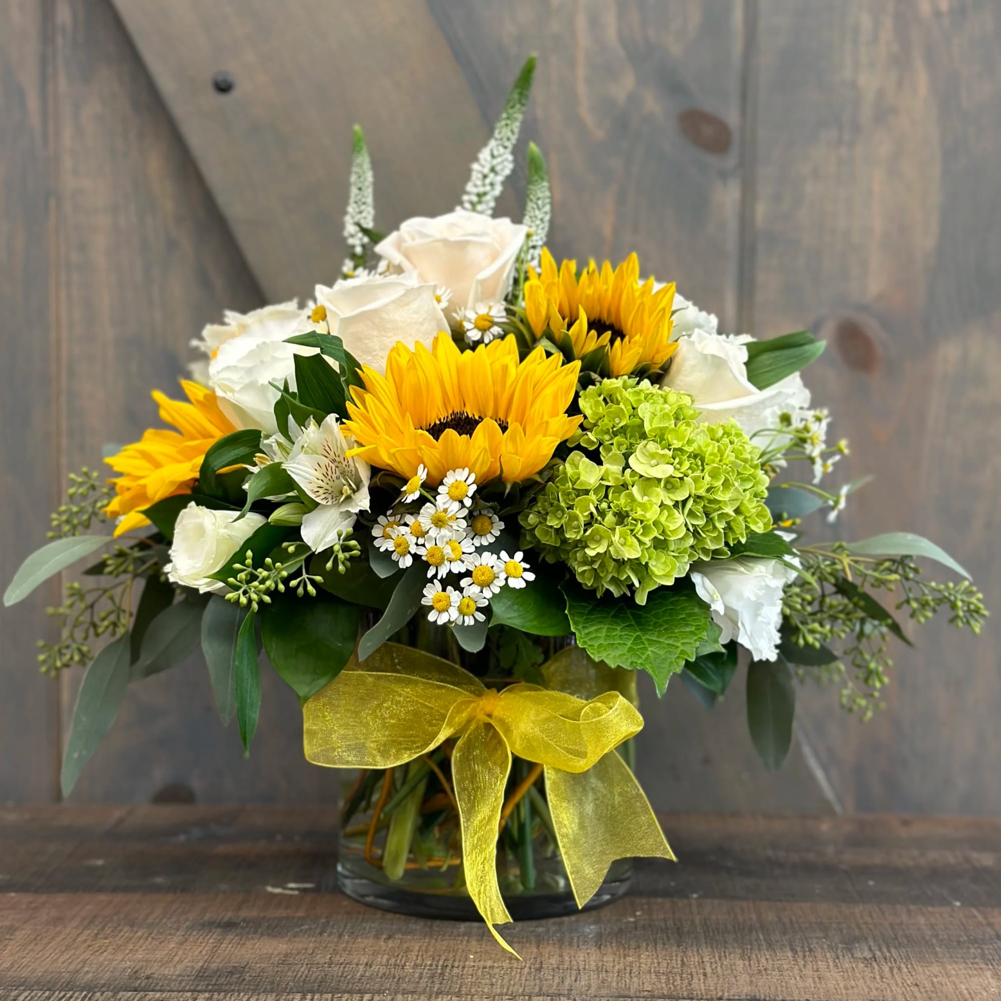 Sunflower and white rose bouquet in a glass vase with a yellow ribbon