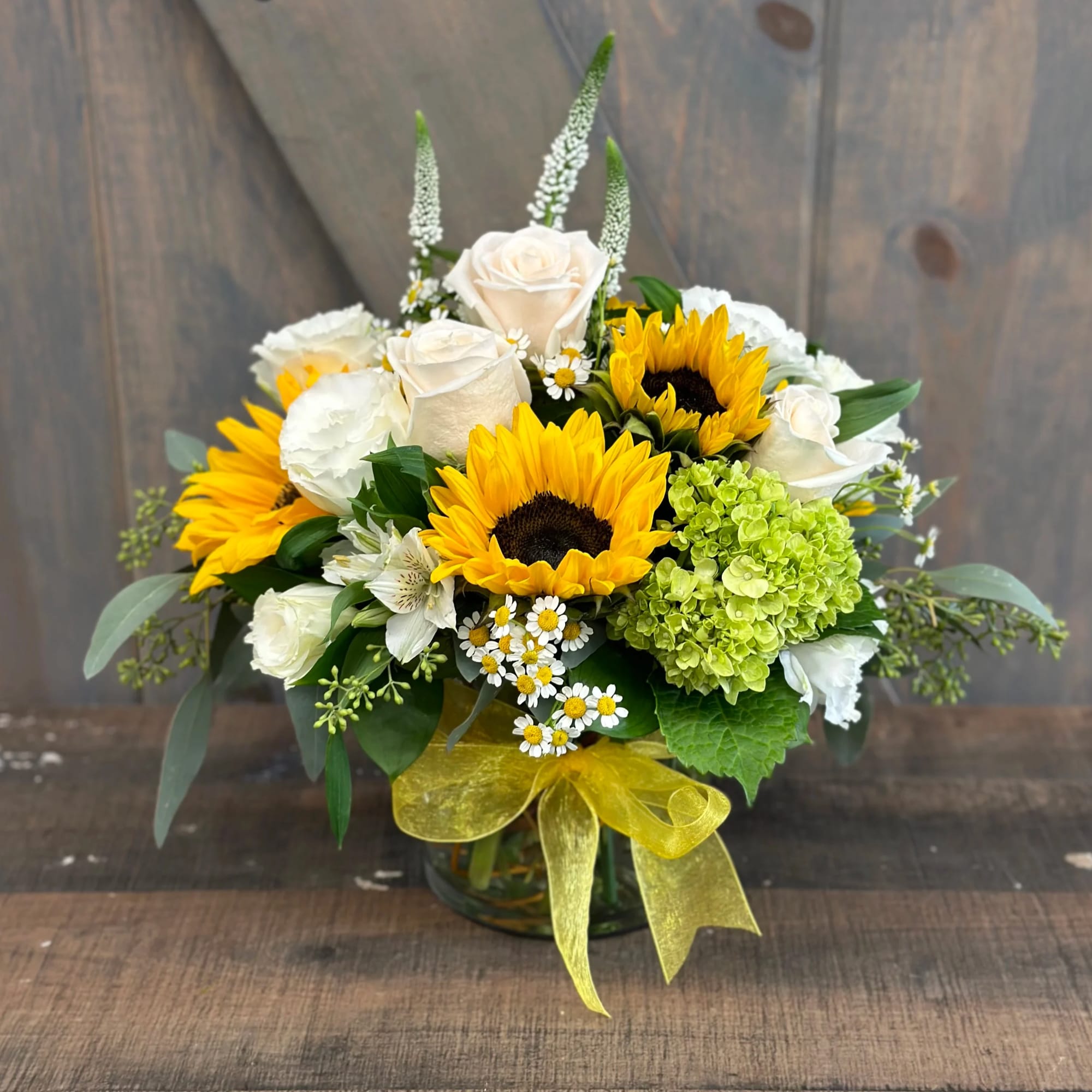 Bouquet of sunflowers, white roses, and green hydrangea in a glass vase