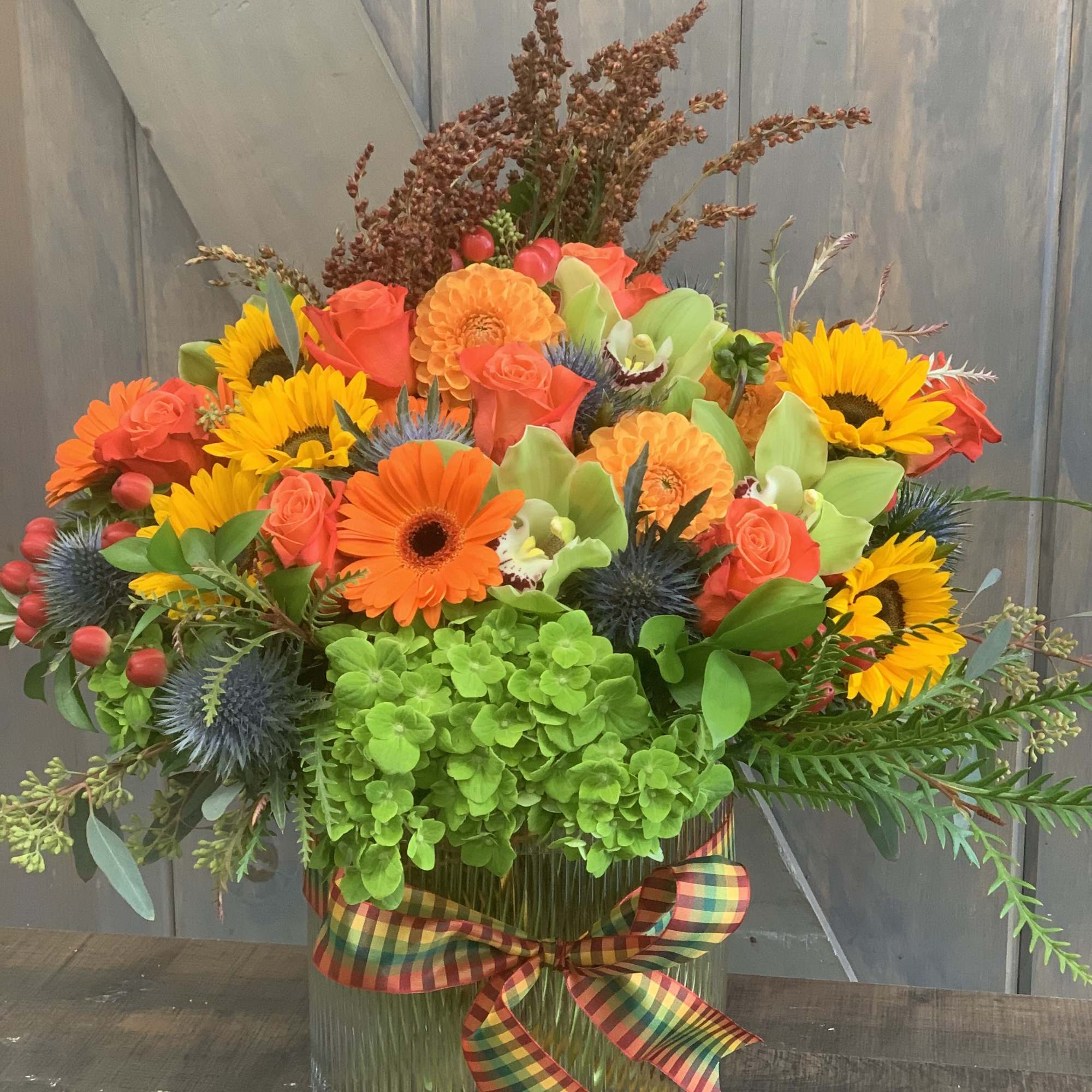 Bright mixed flower arrangement in a glass vase with a plaid ribbon