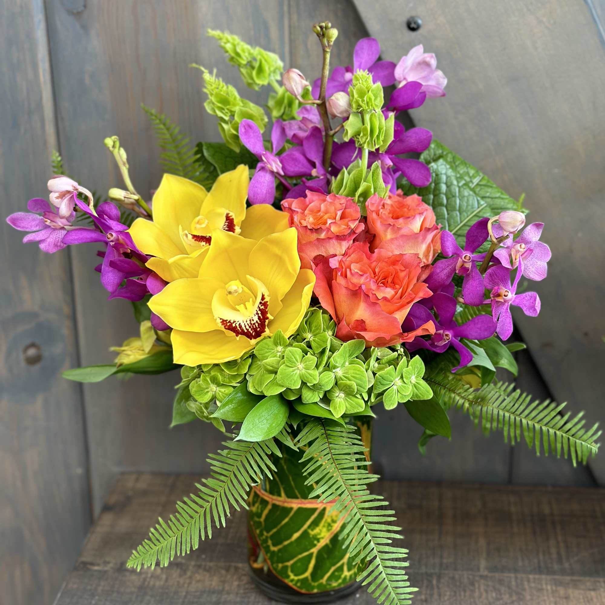 Bright bouquet of yellow orchids, coral roses, and purple orchids in a vase