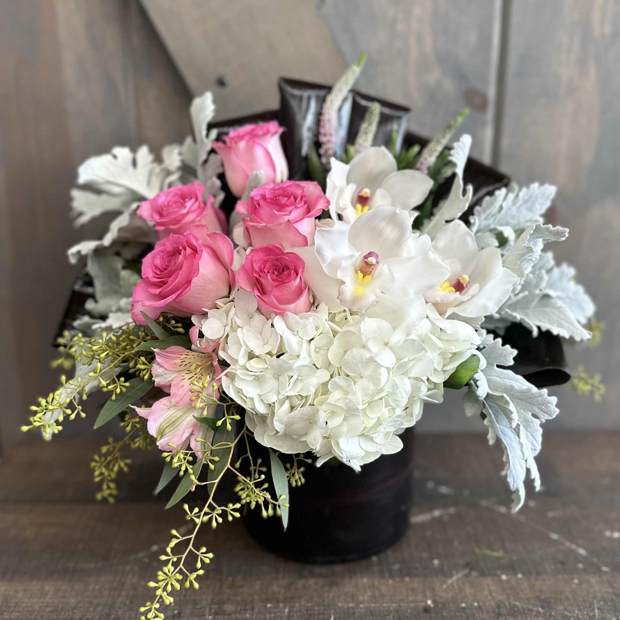 Pink roses and white orchids arranged with white hydrangea in a black box