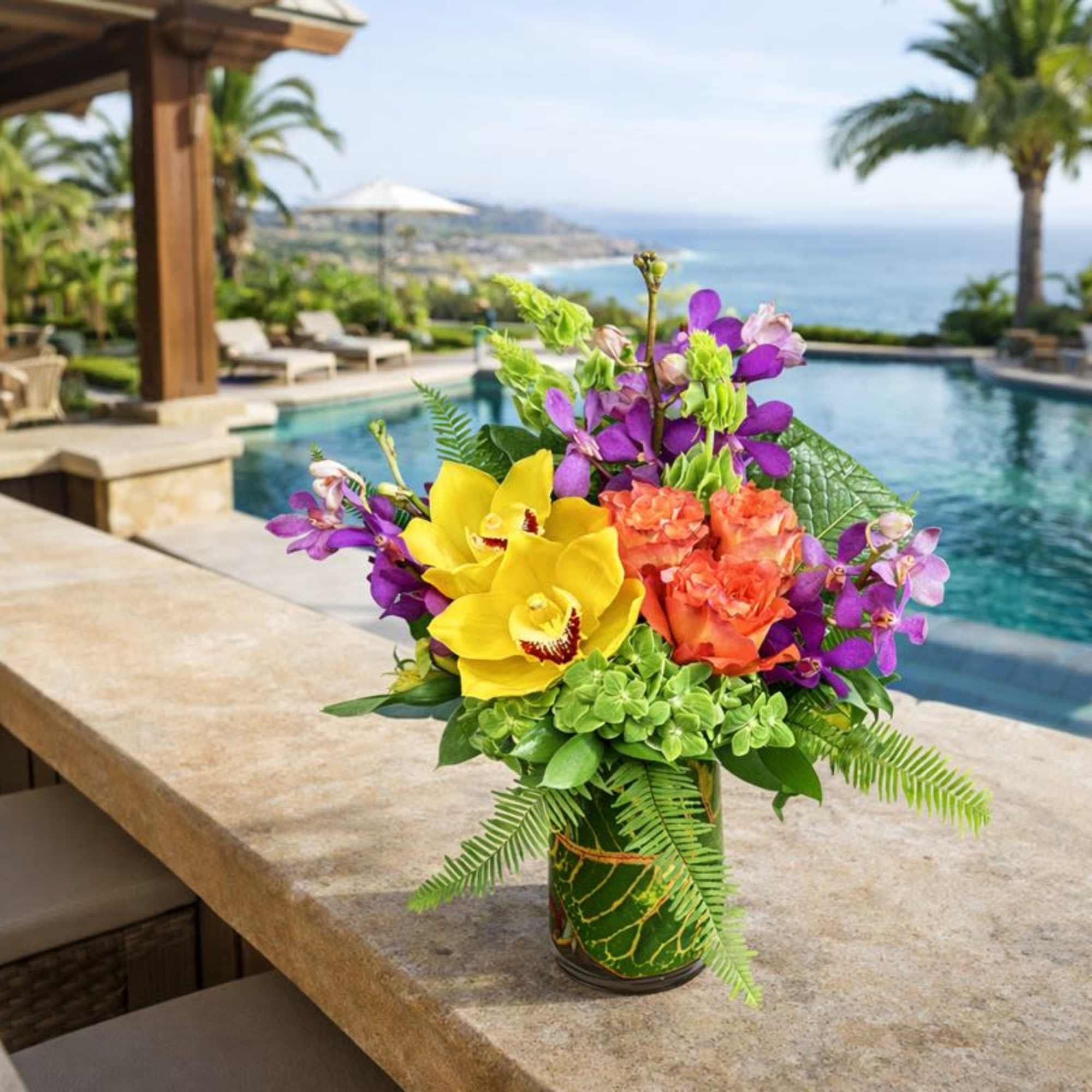 Tropical bouquet with yellow orchids, purple flowers, and orange blooms in a glass vase
