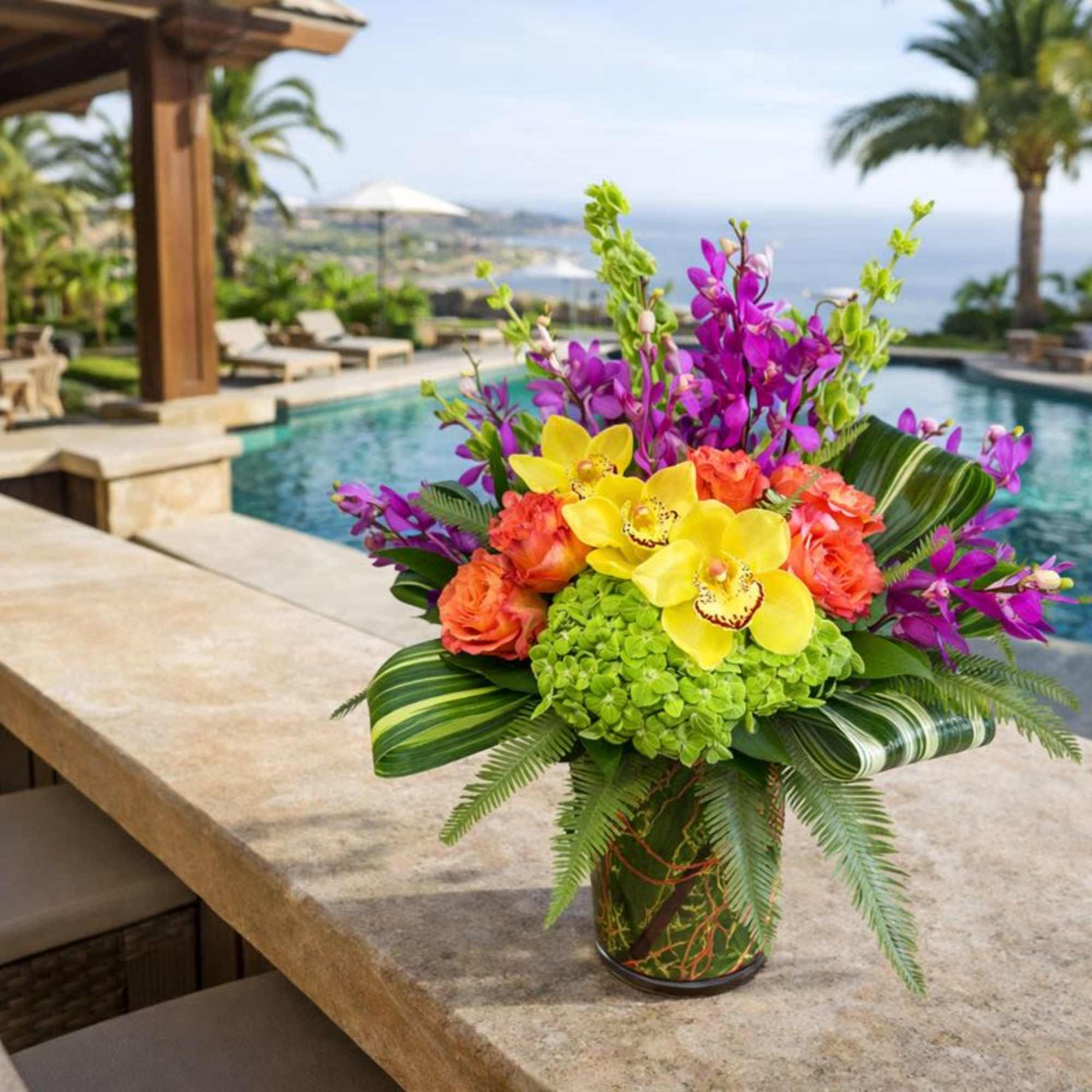 Tropical bouquet with yellow orchids, orange roses, and purple blooms in a vase