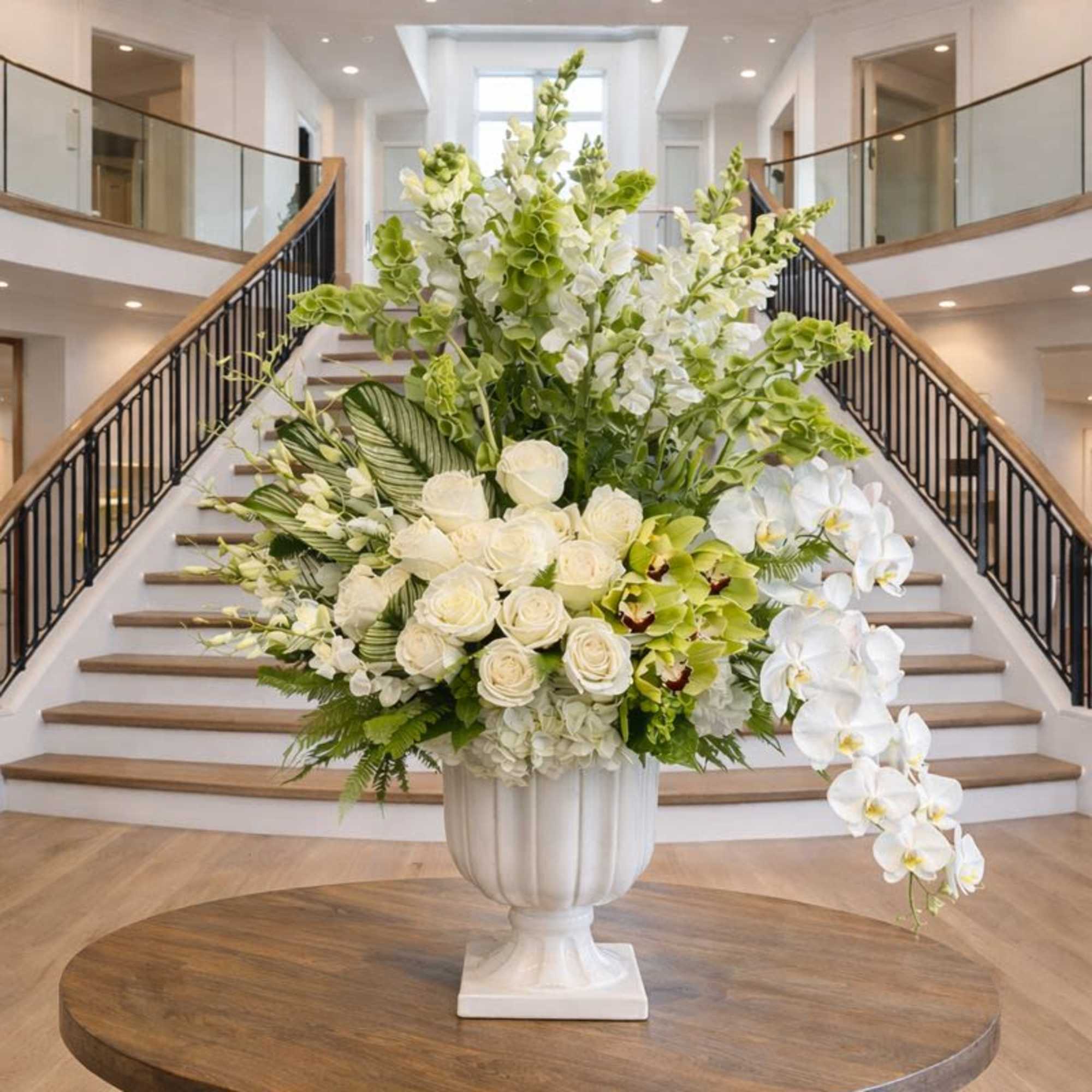 Large white floral arrangement in a pedestal vase with cascading orchids