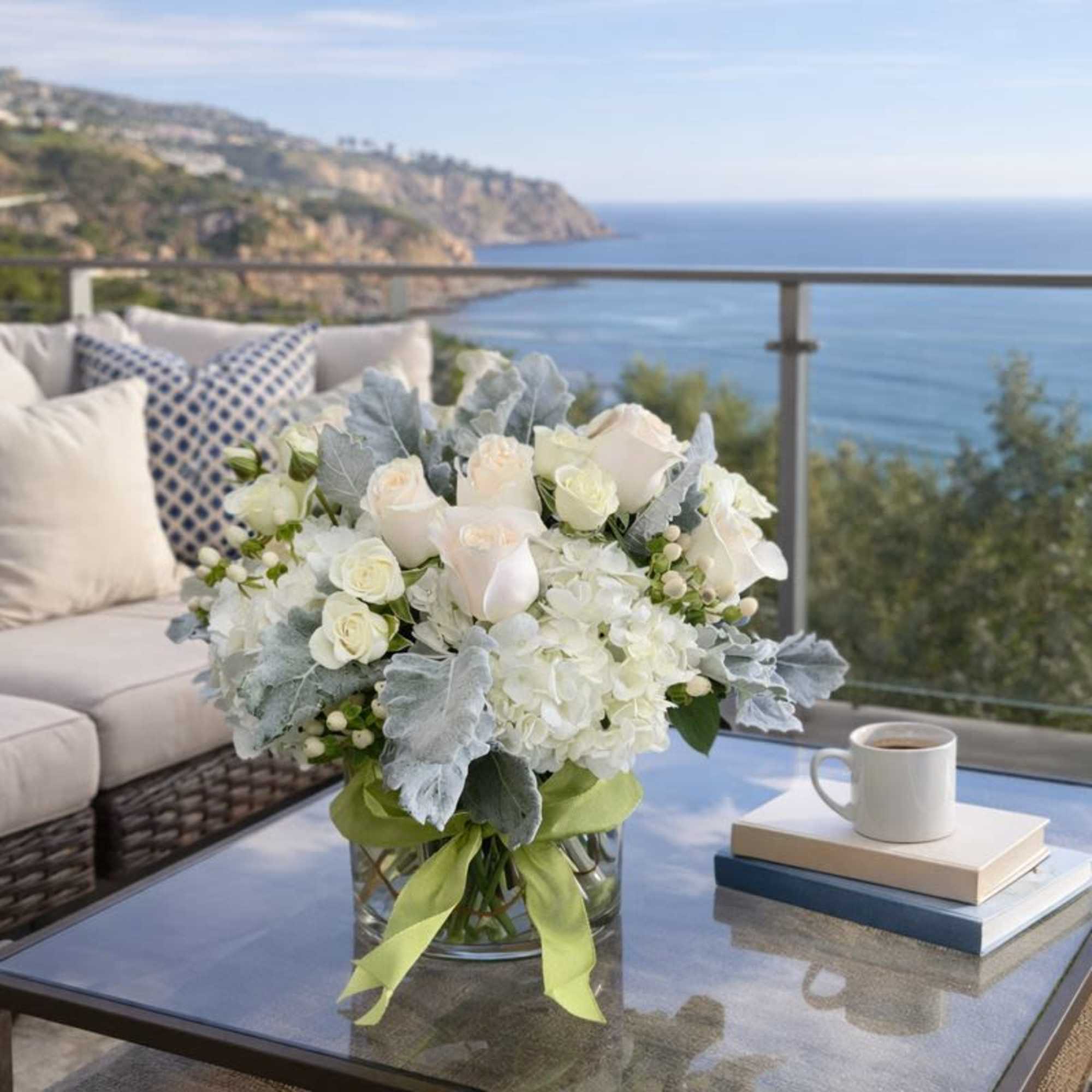 White roses and hydrangeas in a glass vase with a green ribbon
