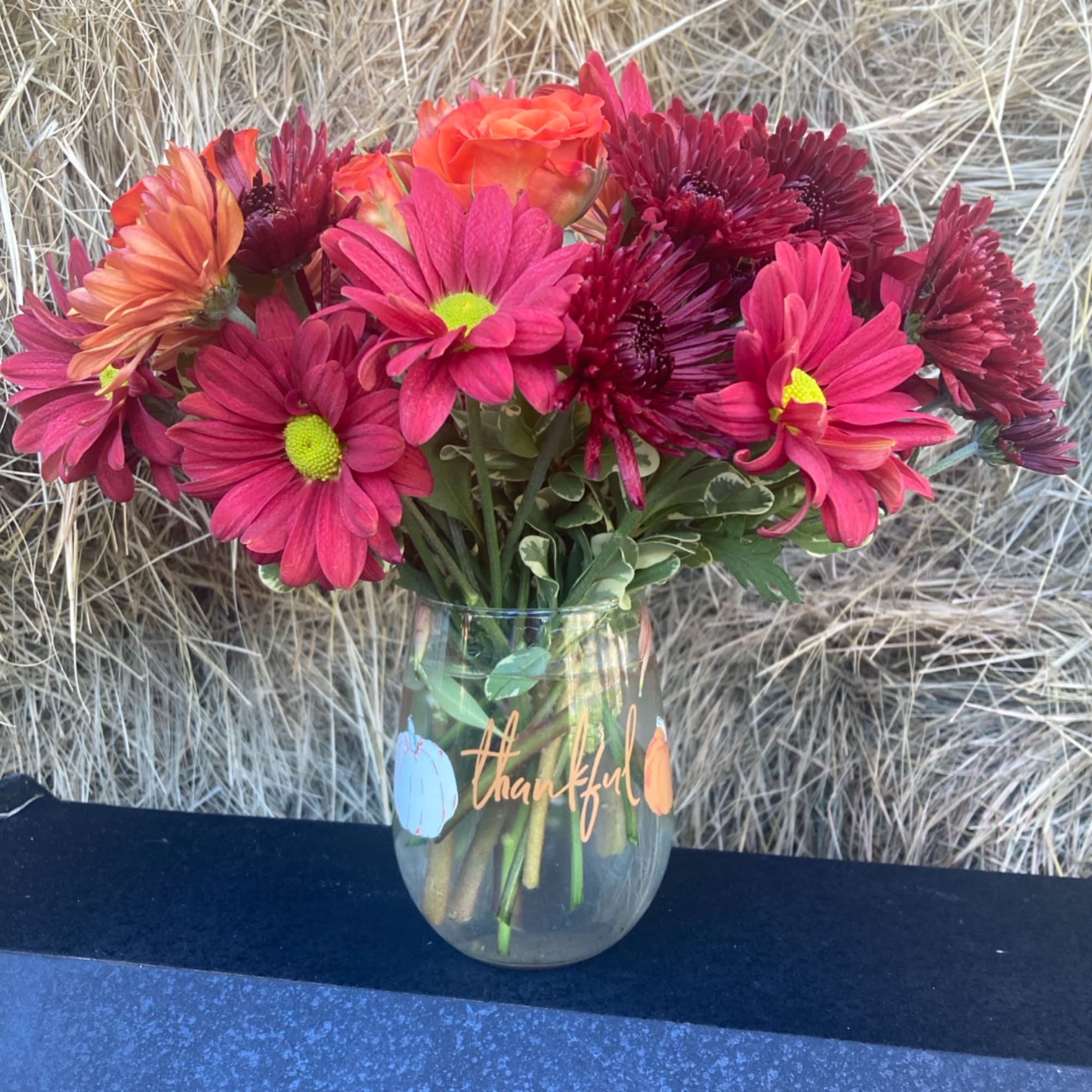 Pink and orange daisy bouquet in a glass vase with a thankful message