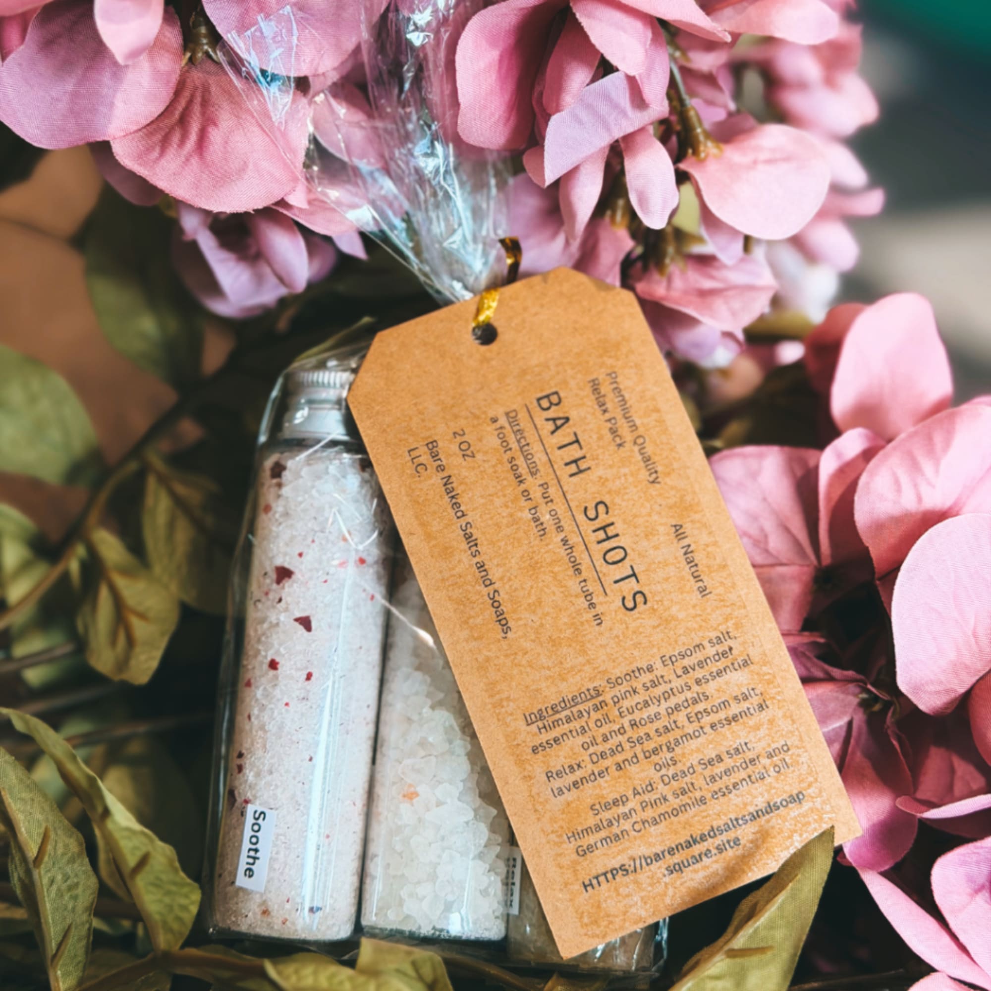 Pink flowers surround a bath salts gift set with a kraft tag.