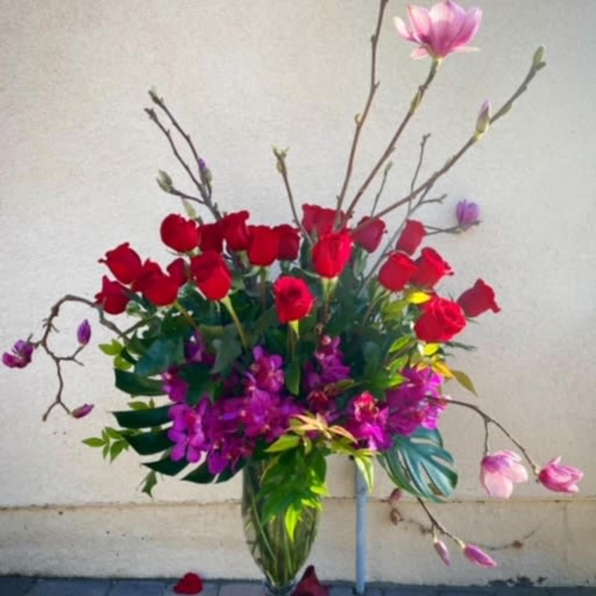Tall bouquet of red roses and pink magnolia blossoms in a glass vase