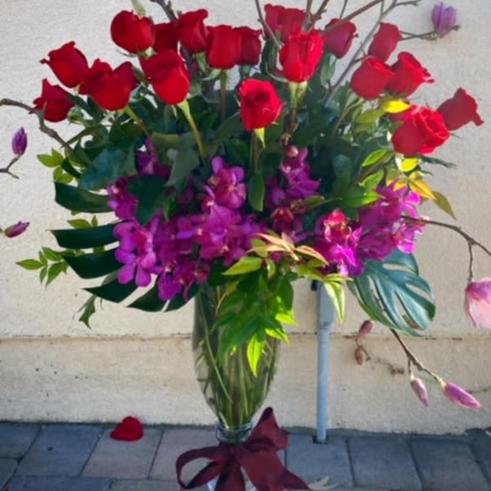 Tall vase arrangement of red roses and purple orchids with a burgundy ribbon