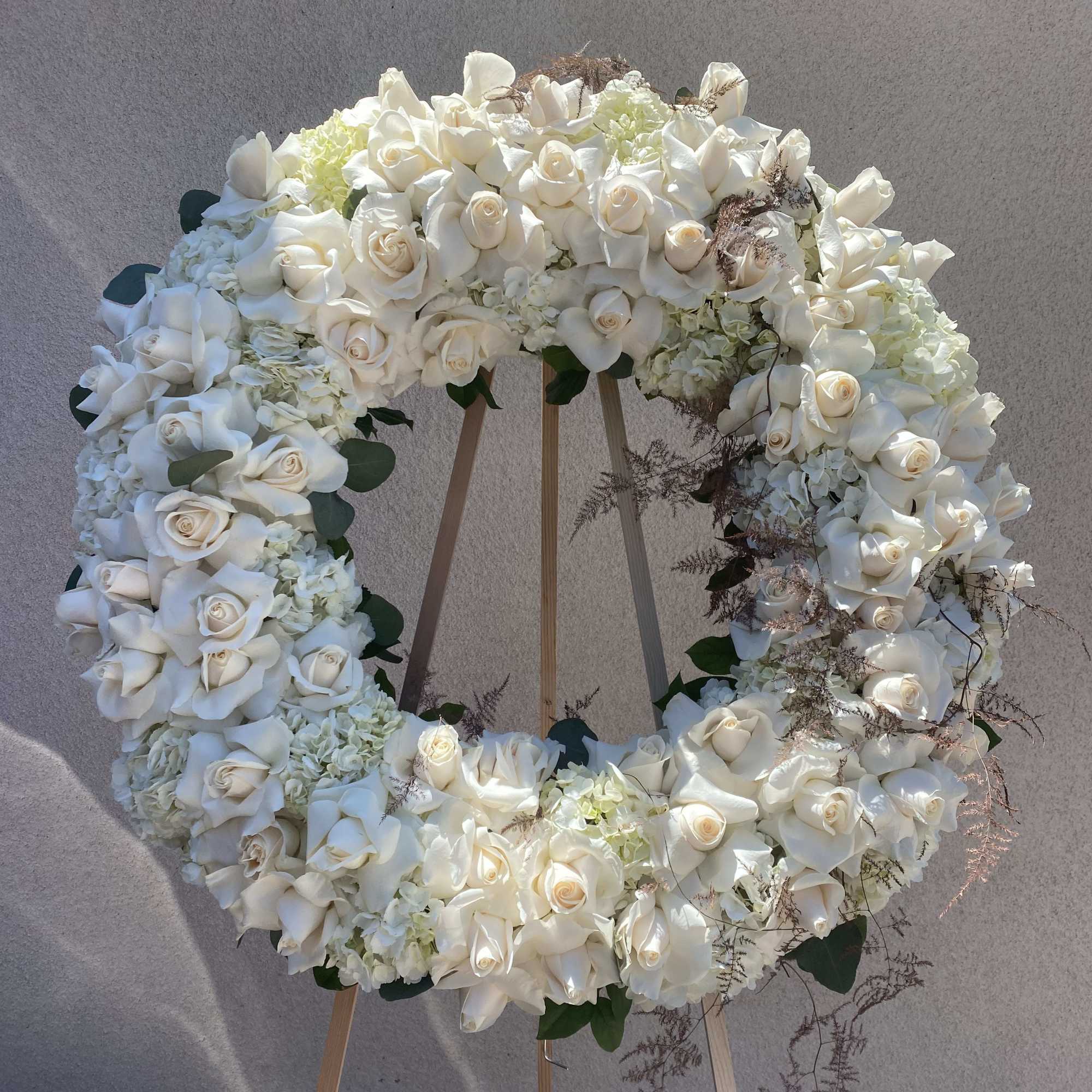 Large white floral wreath on a wooden stand