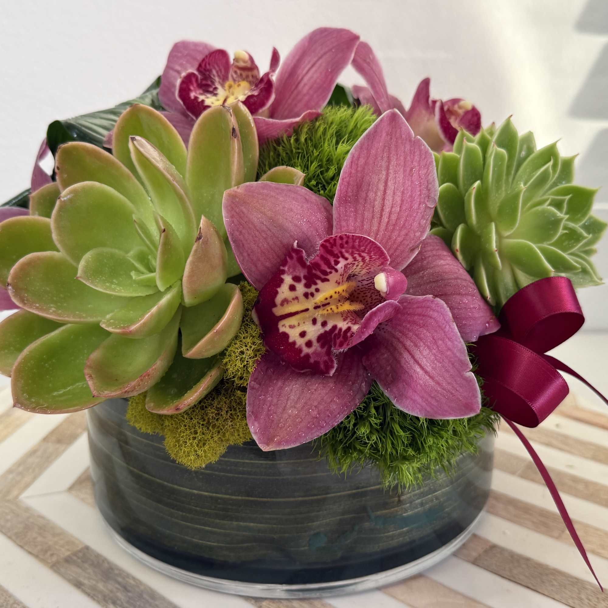 Succulent and orchid arrangement in a round glass bowl with a ribbon