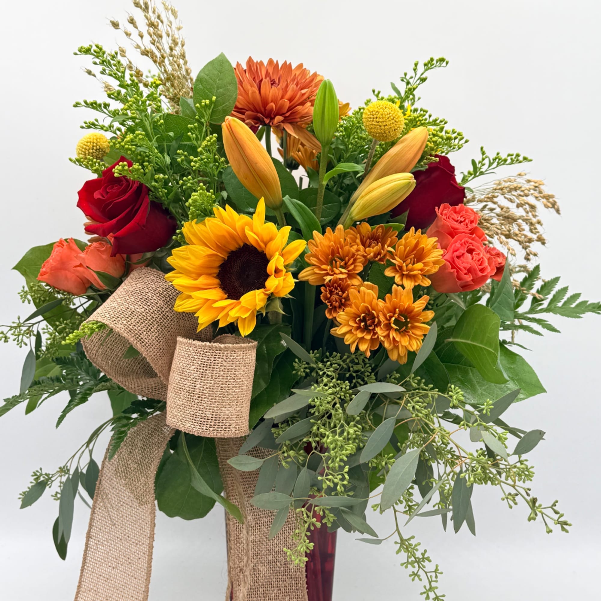 Mixed bouquet with sunflowers, roses, lilies, and orange mums in a vase with burlap ribbon