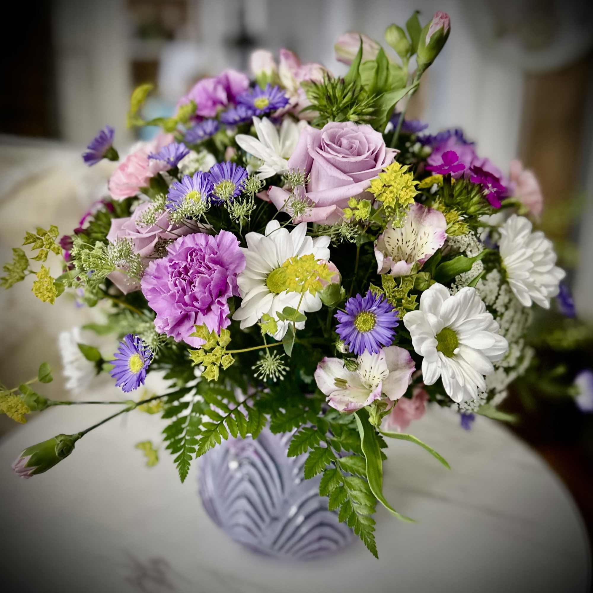 Mixed bouquet of pink, purple, and white flowers in a lavender vase
