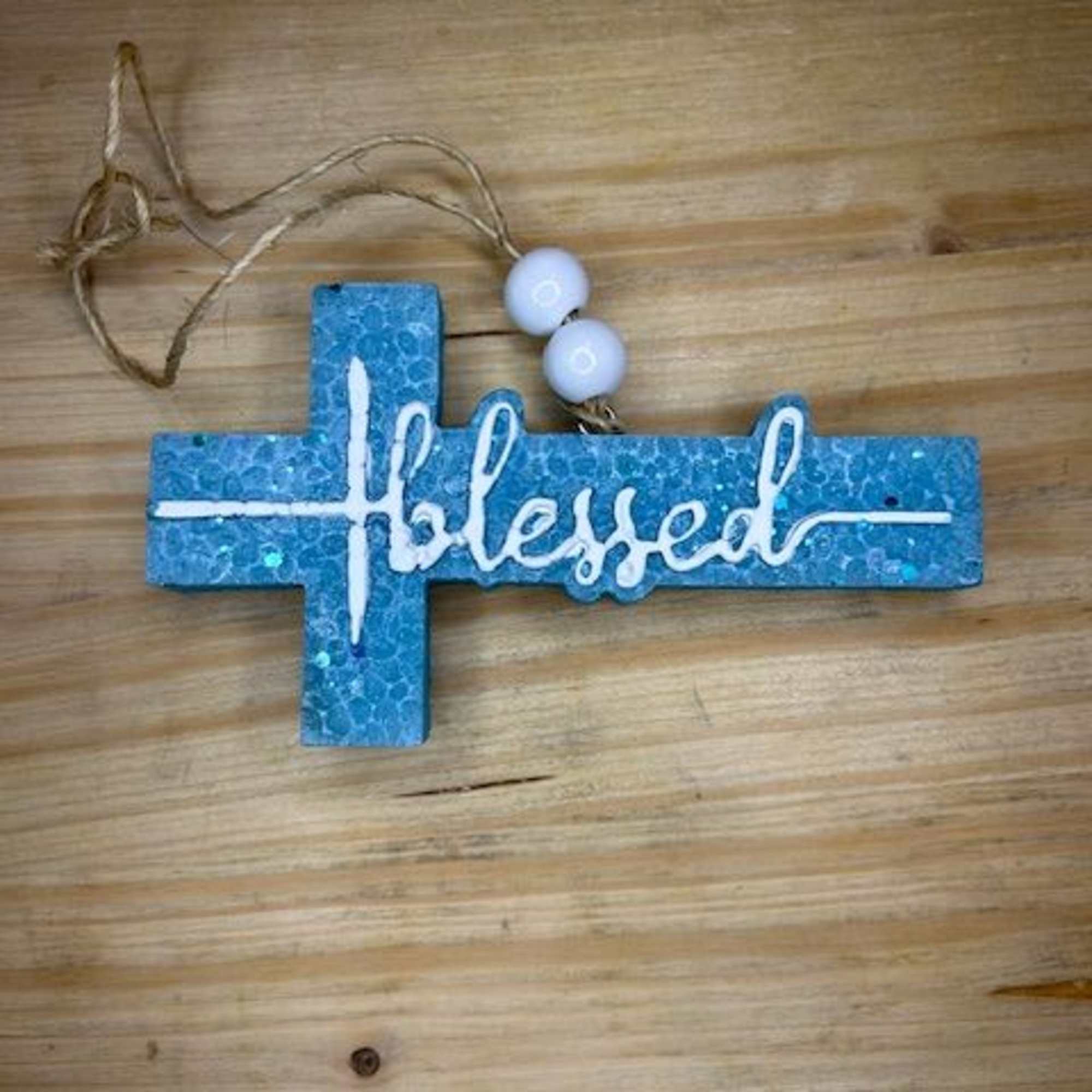 Blue cross ornament with the word blessed on a wooden surface