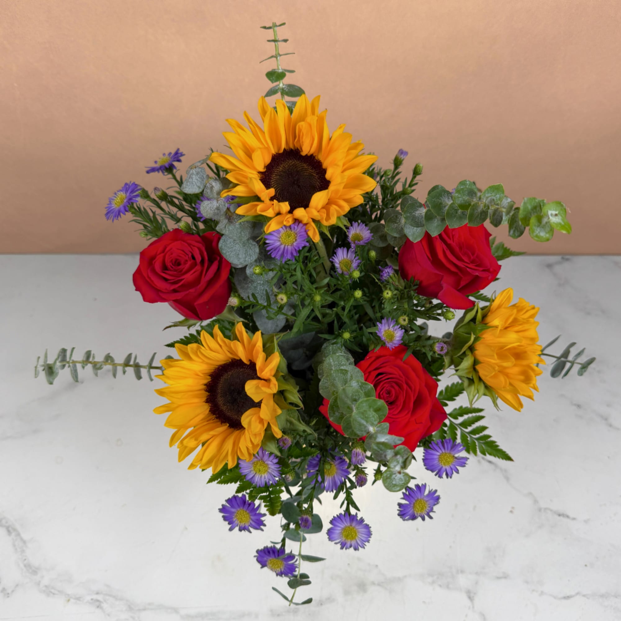 Sunflowers, red roses, and purple daisies in a compact bouquet