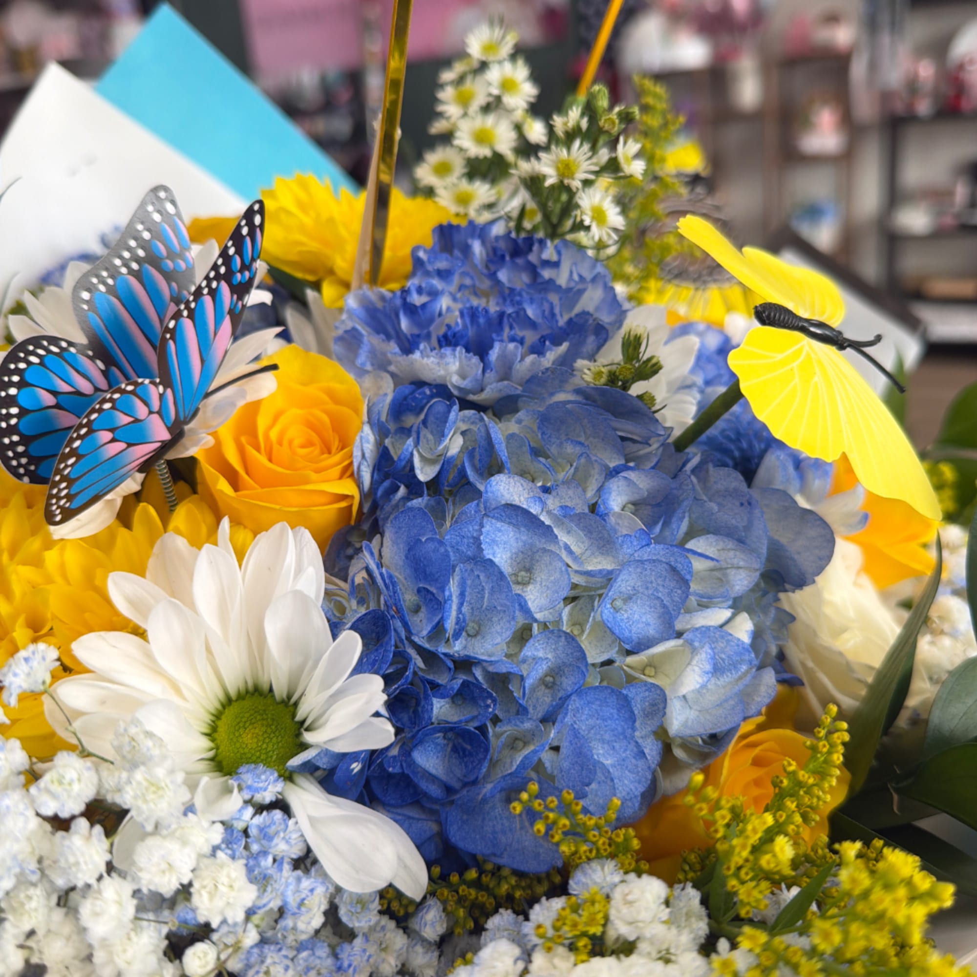 Bouquet of blue hydrangeas, yellow roses, and white daisies with butterfly picks