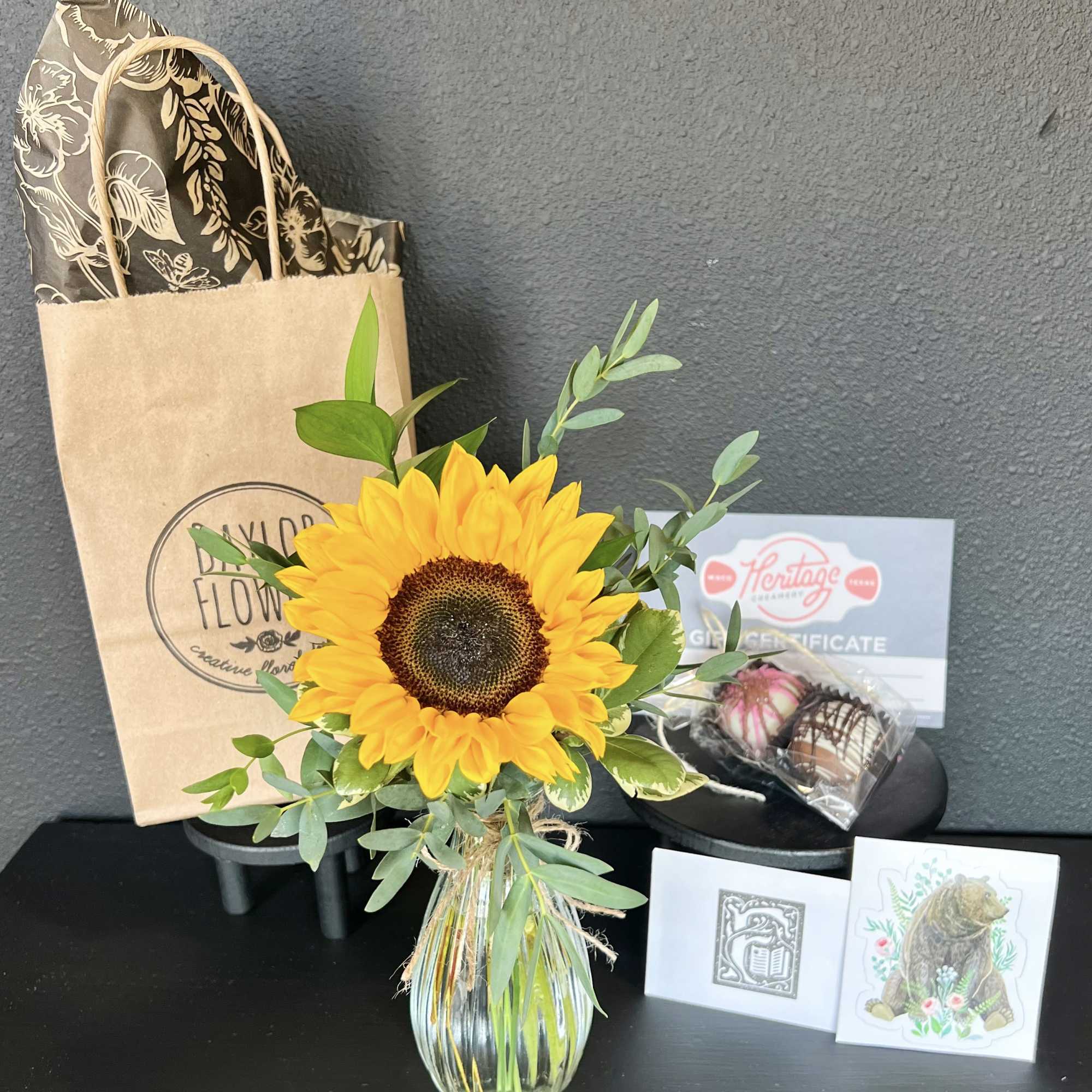 Sunflower arrangement in a glass vase with a gift bag and chocolates