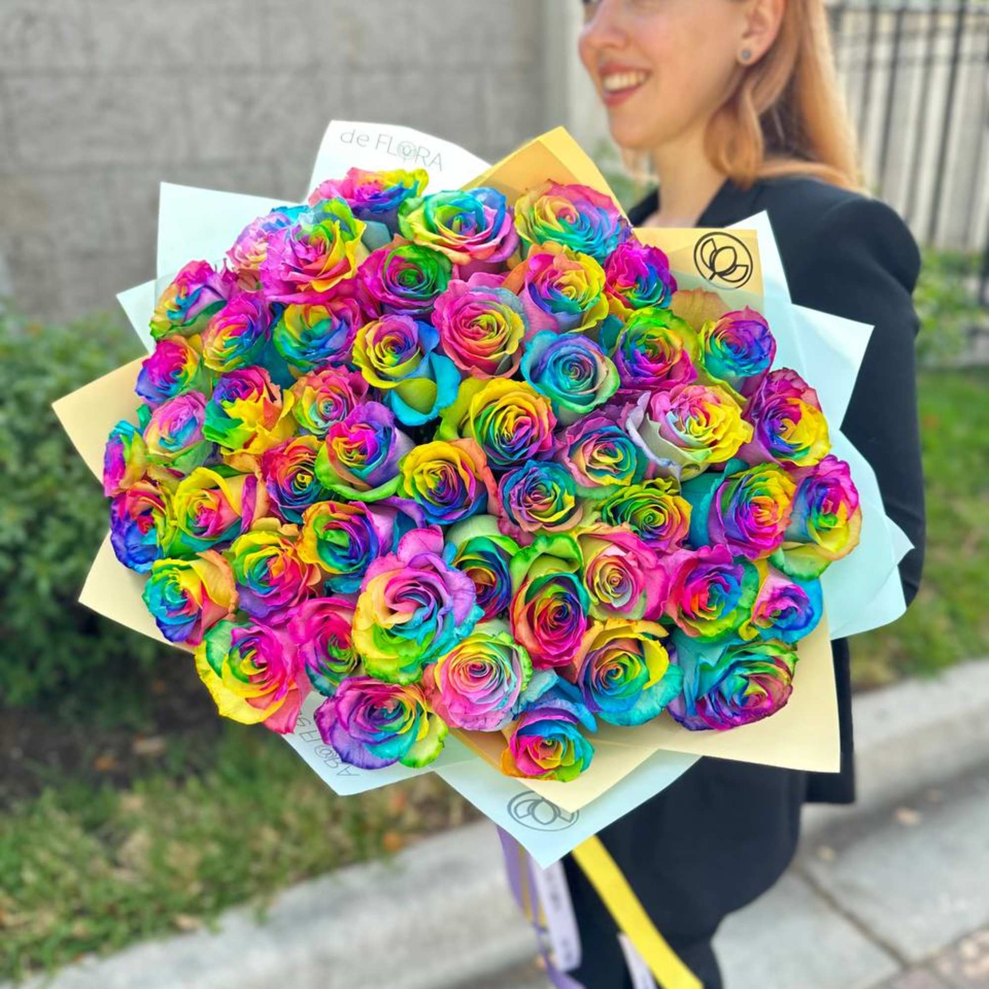 Large bouquet of rainbow-colored roses wrapped in pastel paper