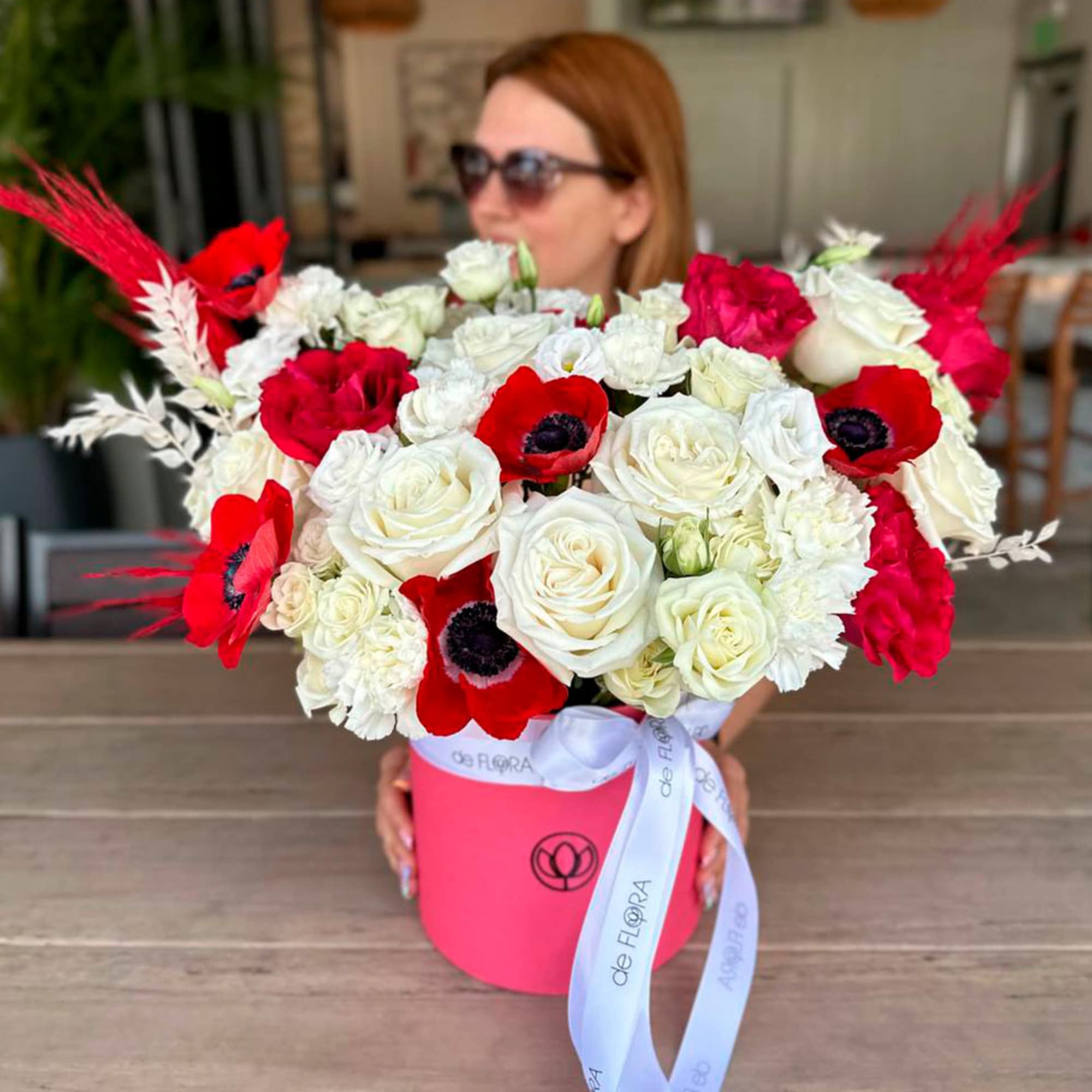 Bouquet of red and white roses with red anemones in a pink hatbox