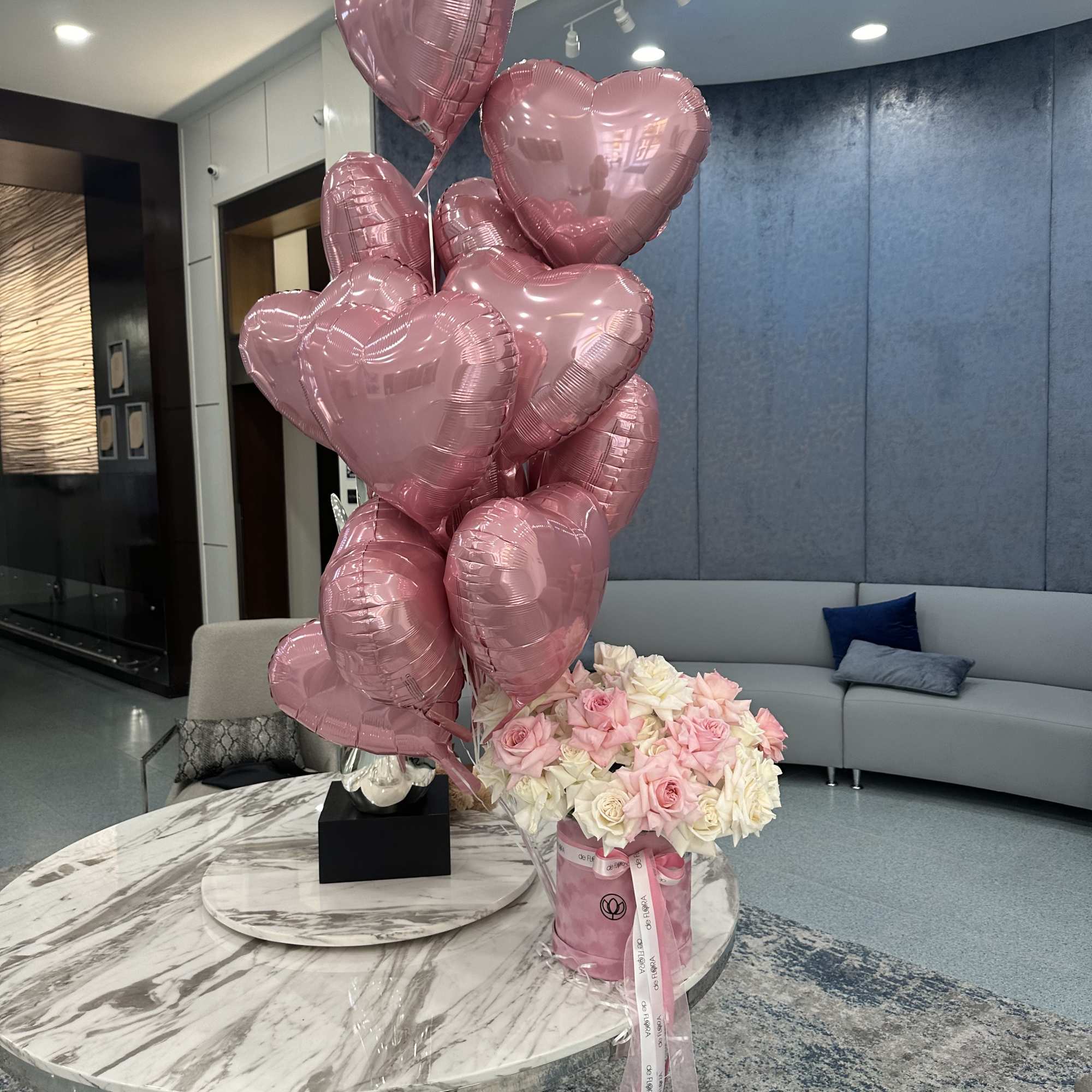 Pink heart balloons beside a box of pink and white roses