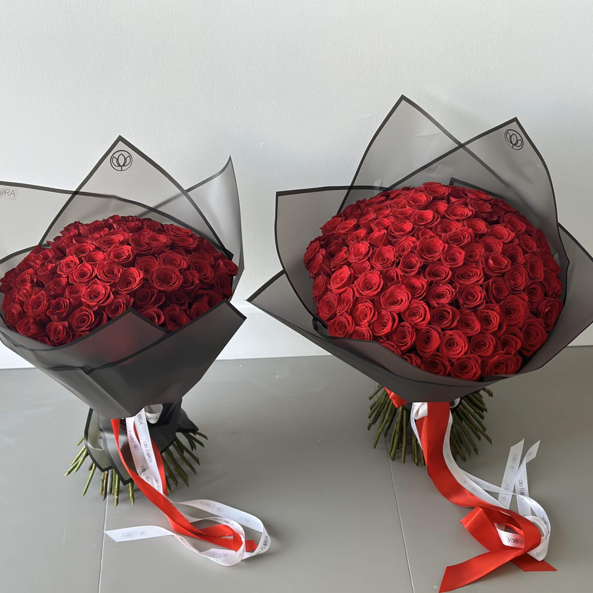 Two large domed bouquets of red roses wrapped in black paper with long red and white ribbons