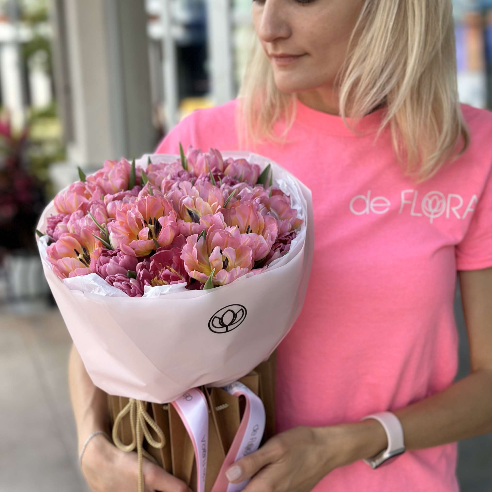 Woman holding a bouquet of pink and peach tulips wrapped in white paper