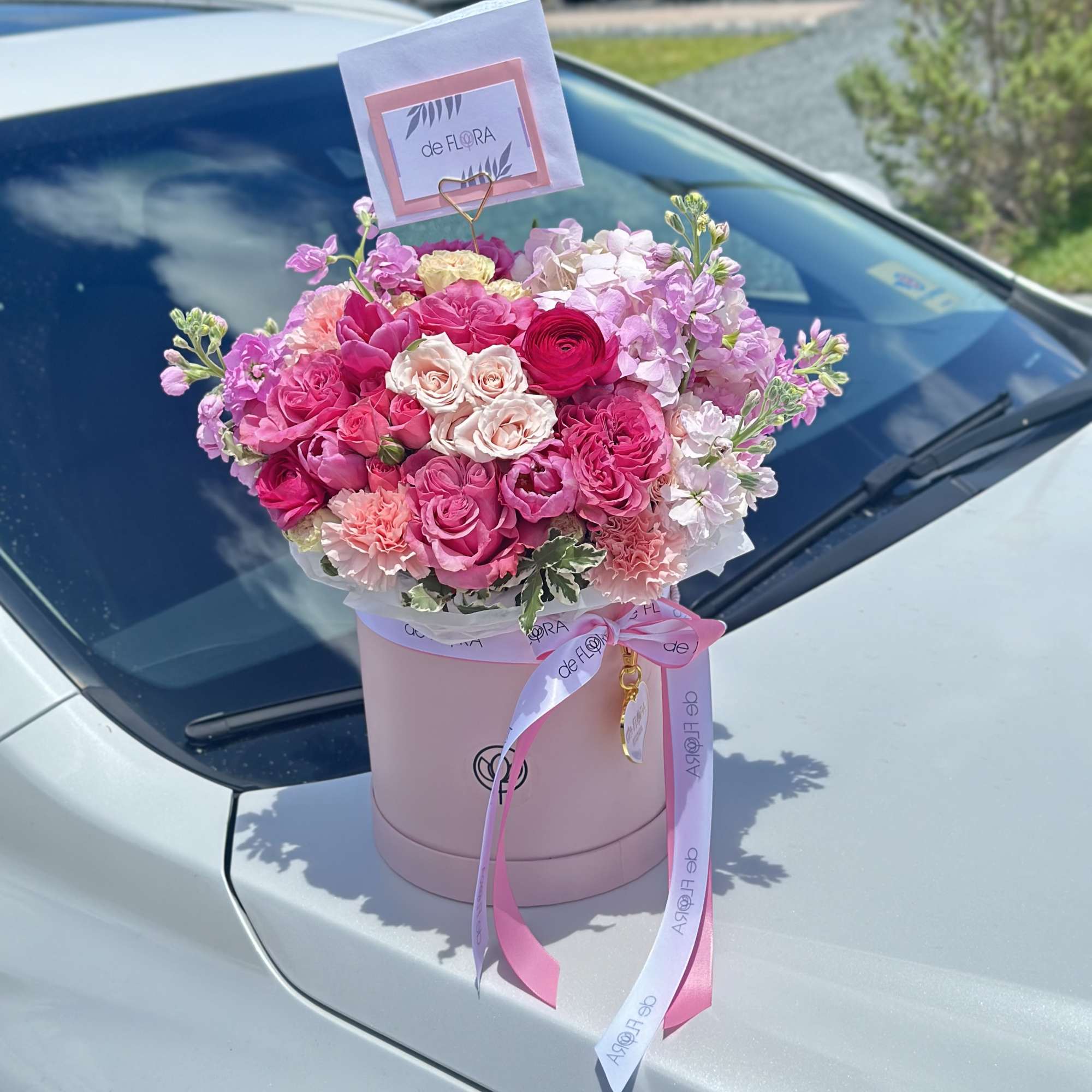 Pink and white flower arrangement in a round box on a car hood