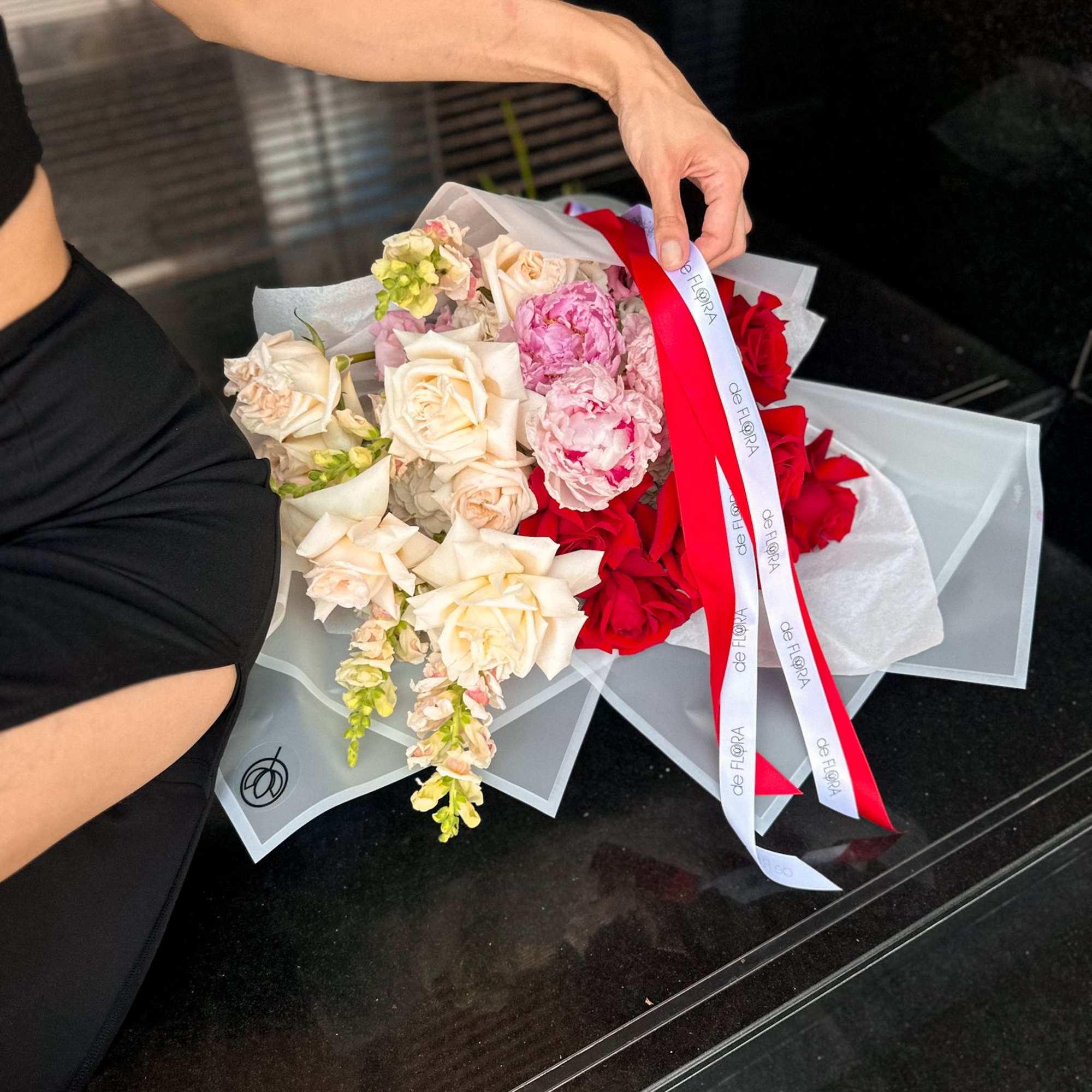 Handheld bouquet of cream, pink, and red roses wrapped in translucent paper