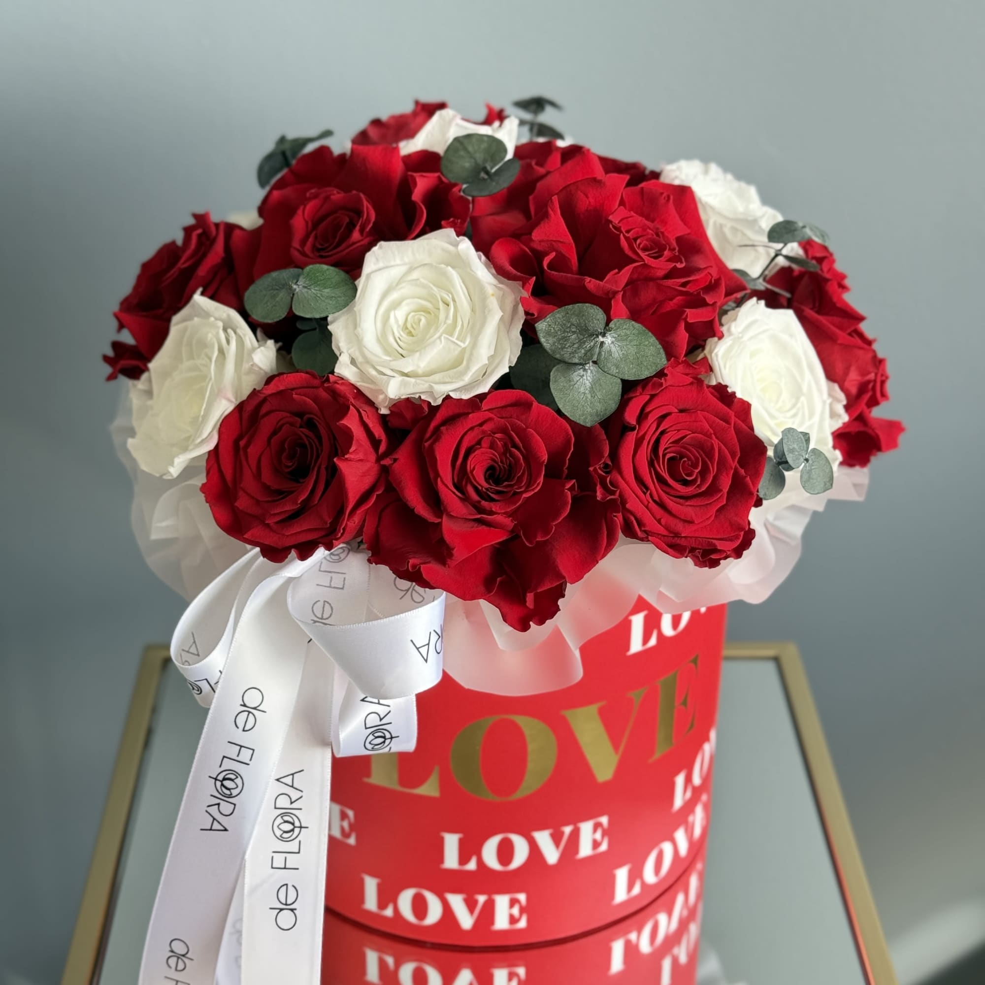 Red and white roses arranged in a red box with a white ribbon