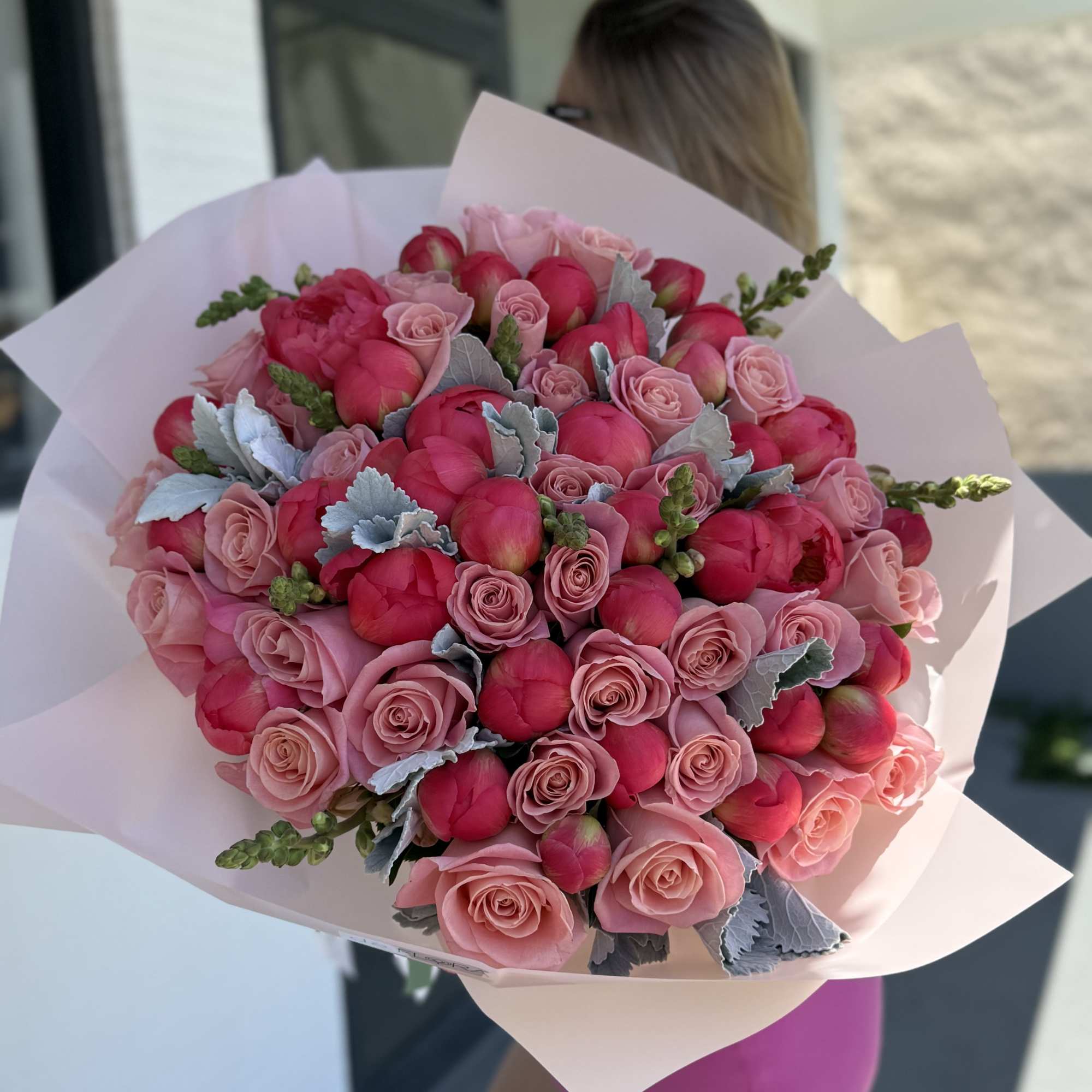 Large pink bouquet of roses and peony-like blooms wrapped in pale paper