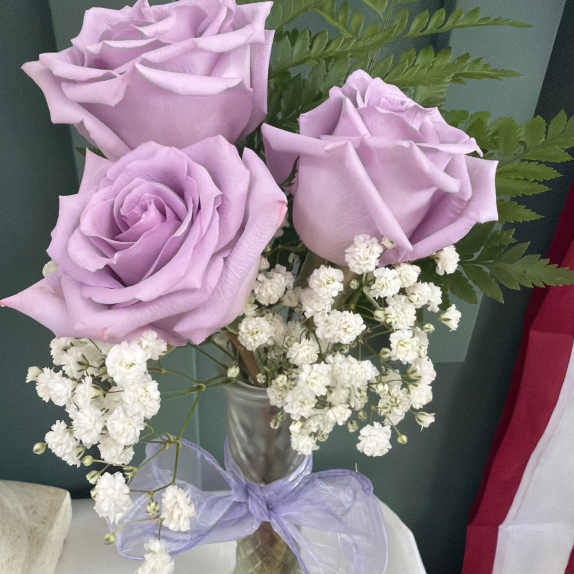 Lavender roses with white baby's breath in a clear vase tied with a purple ribbon