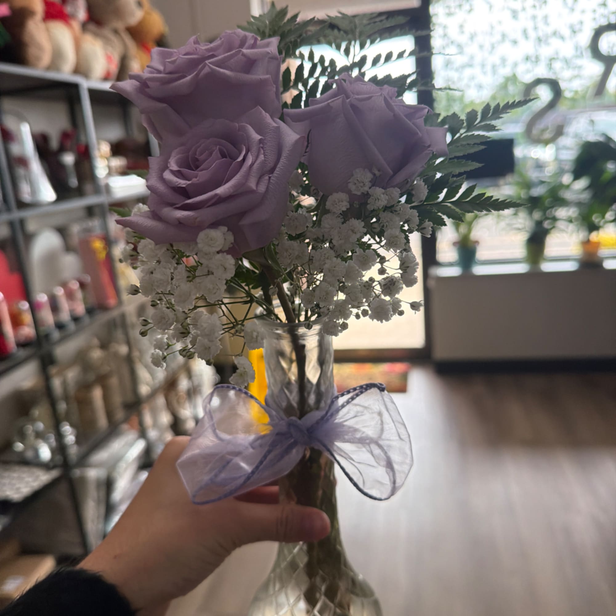 Handheld bouquet of lavender roses and white baby's breath in a glass vase