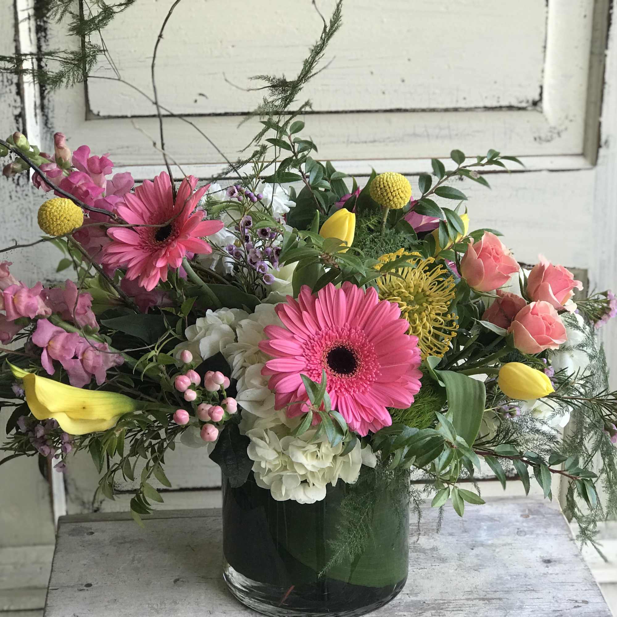 Mixed bouquet in a glass vase with pink gerberas, yellow tulips, and roses