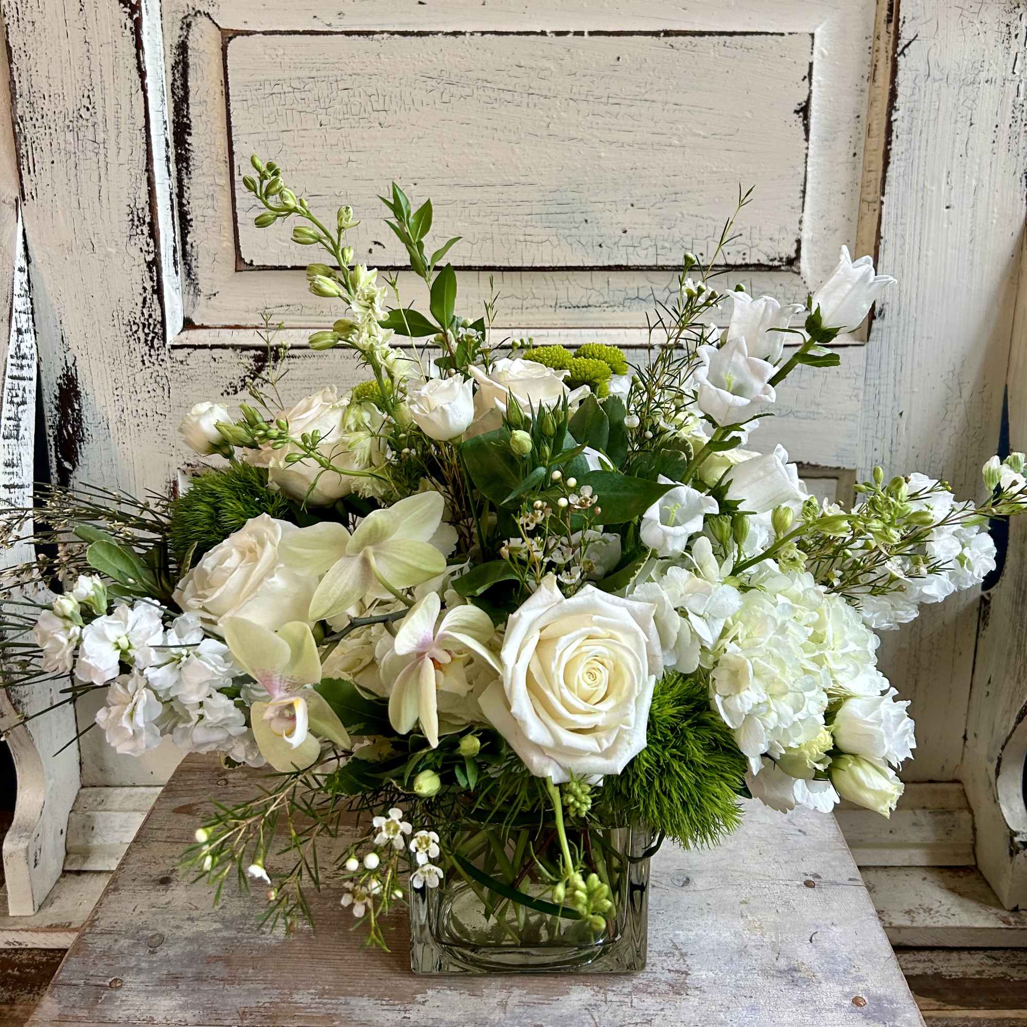 White roses and orchids arranged in a square glass vase