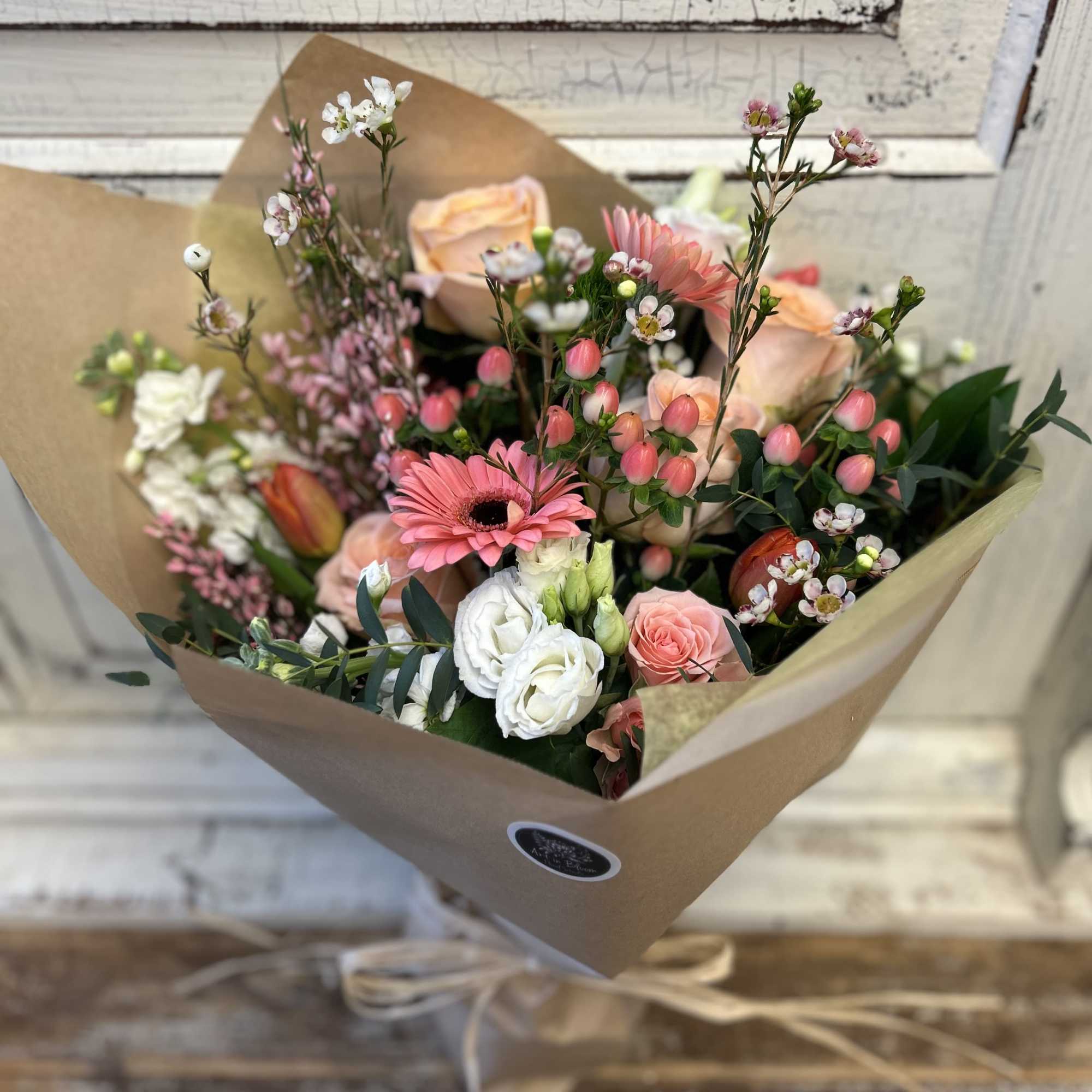 Hand-tied bouquet of pink and white flowers wrapped in brown paper